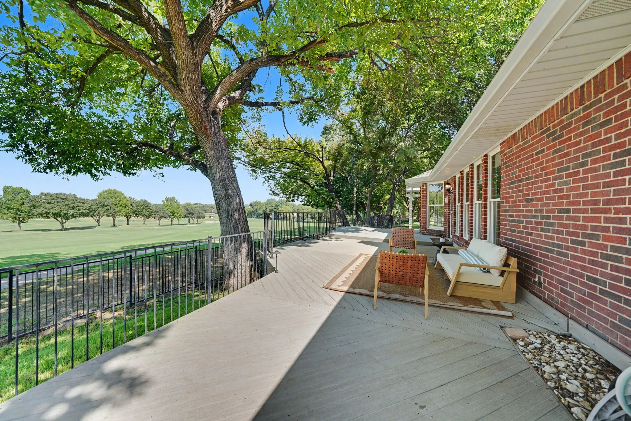 Expansive outdoor deck with wood-finish flooring, bordered by a black metal railing and mature trees