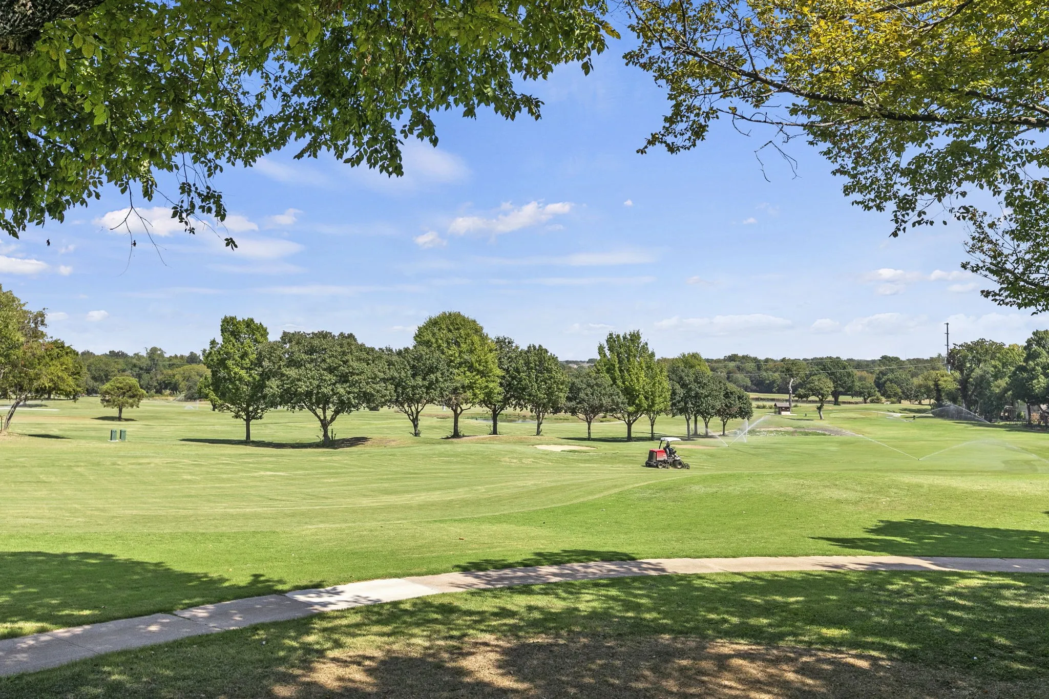 Expansive view of the manicured golf course greens, mature trees, and a paved walking pathways