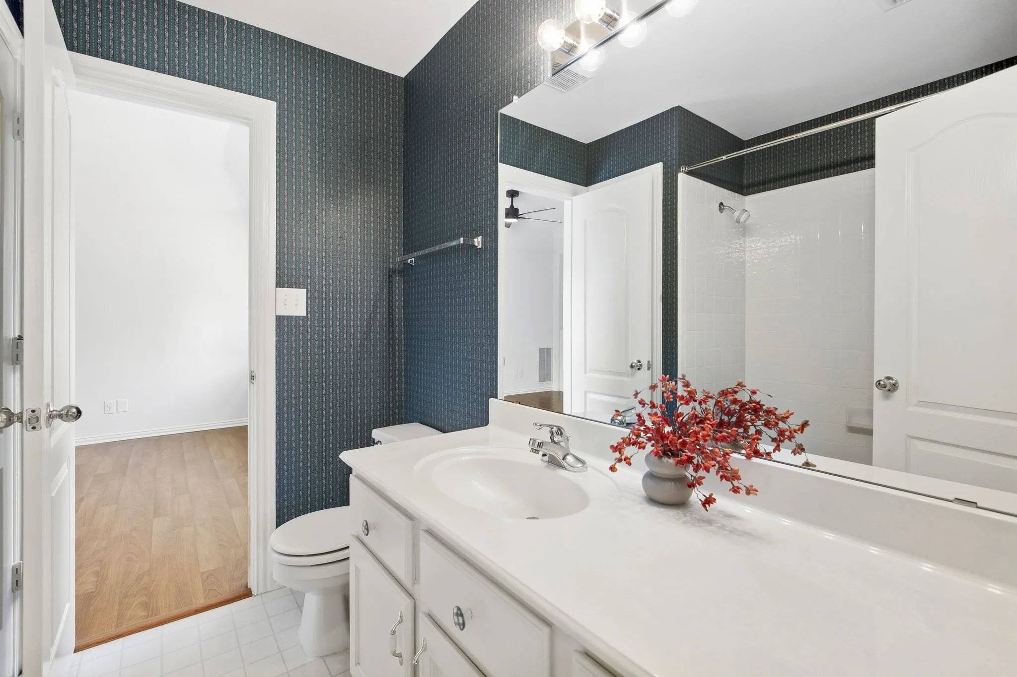 Upstairs Bathroom shared with Loft and Guest Bedroom 1, featuring a single vanity with a white countertop, chrome fixtures, a combination shower and tub, and patterned wallpaper