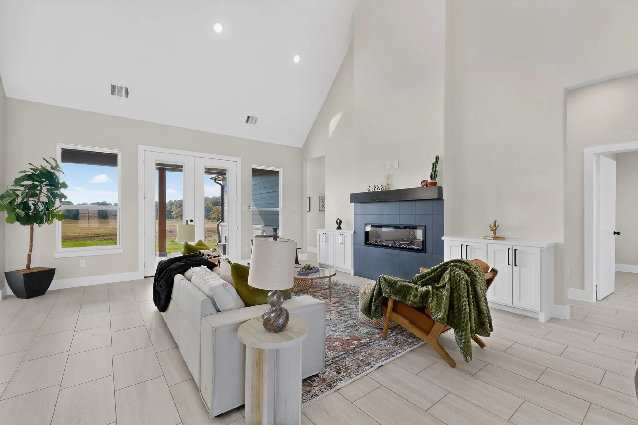 Vaulted ceiling with recessed lighting, large format tile flooring, modern fireplace with blue tile surround, built-in cabinetry, and French patio doors