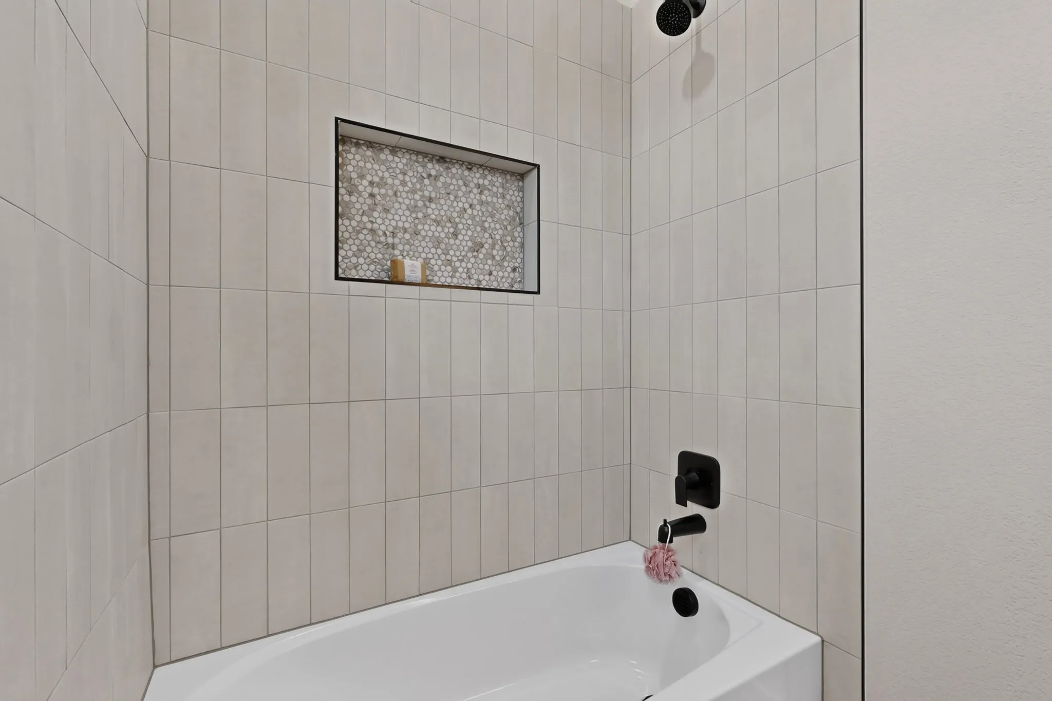 Bathtub with subway tile surround, recessed niche with mosaic tile, and matte black fixtures