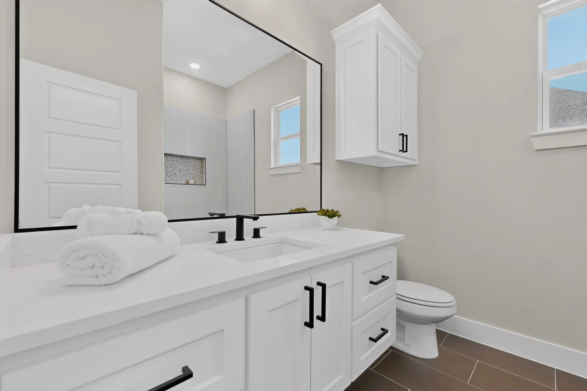White vanity with undermount sink and matte black fixtures, framed mirror, built-in storage cabinet, and tiled flooring