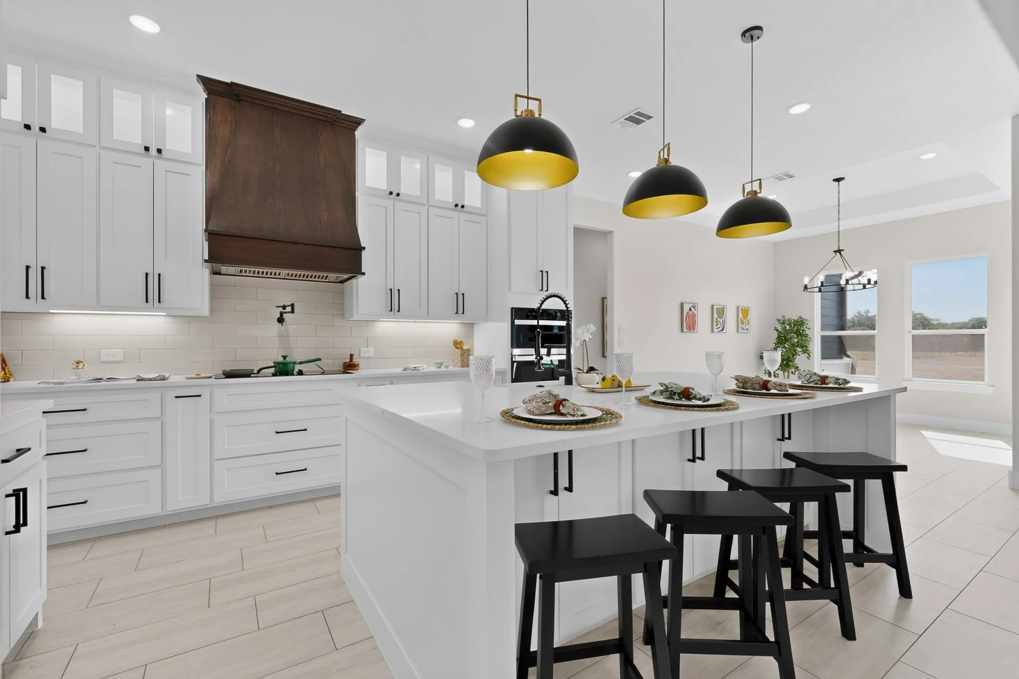 Chef's kitchen featuring white shaker-style cabinetry with black hardware, a large waterfall-edge island with seating for three, stainless steel appliances, and a dark wood-finish range hood
