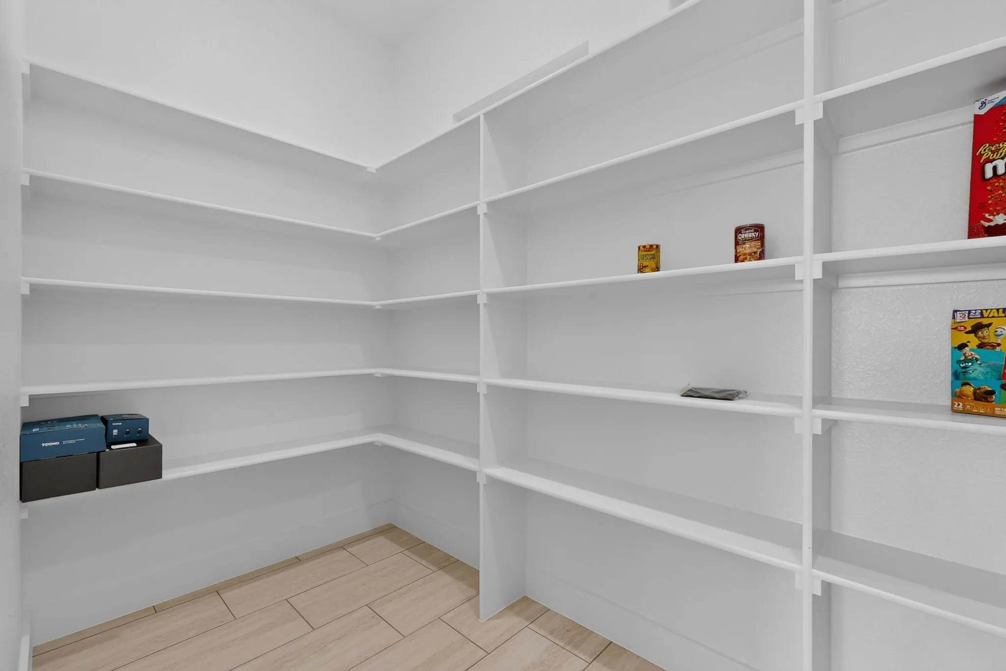 Spacious pantry featuring floor-to-ceiling white shelving with multiple tiers for organized storage, neutral tile flooring, and clean architectural lines throughout