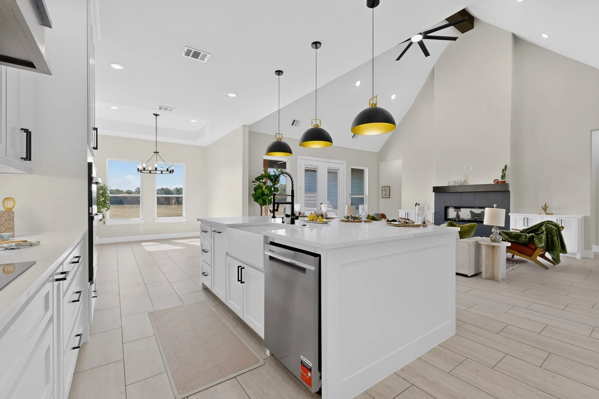 Open-concept living area with vaulted ceilings, a kitchen island featuring a farmhouse sink, integrated stainless steel appliances, and a built-in fireplace