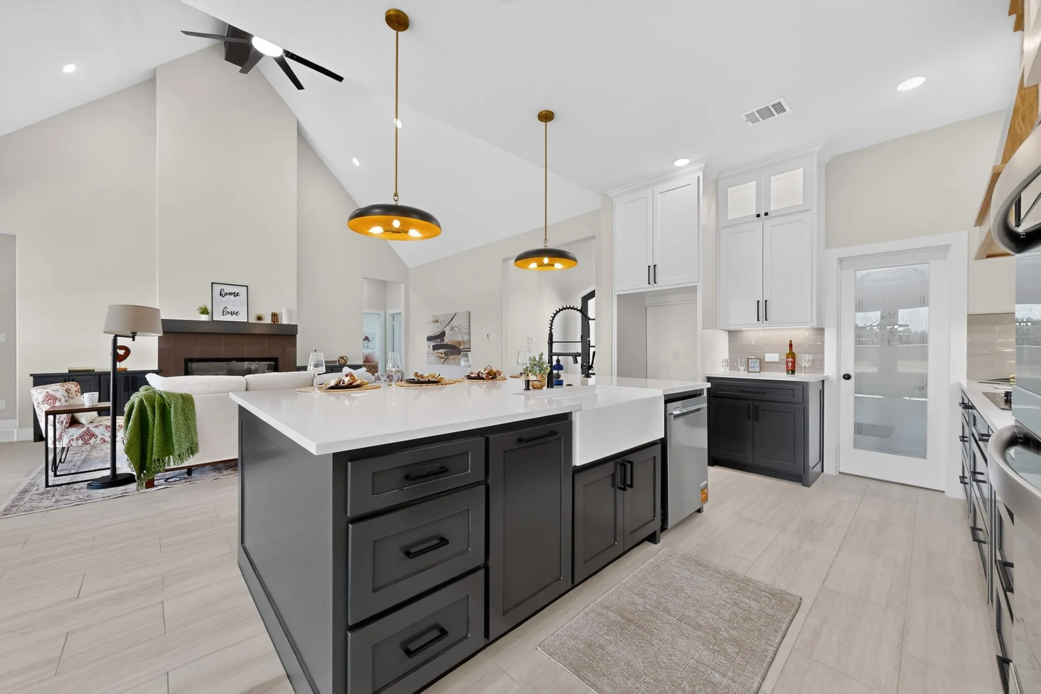 Vaulted ceiling with an exposed beam, kitchen island with a farmhouse sink, stainless steel appliances, and a built-in fireplace