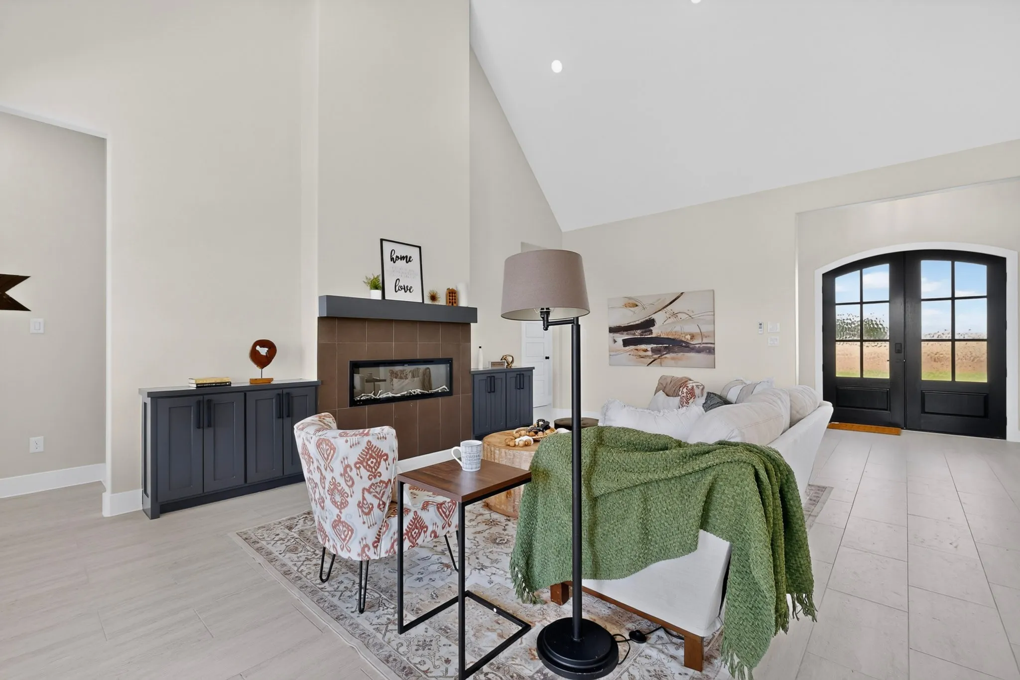 Vaulted ceiling, arched double doors, tiled fireplace with built-in insert, light-toned wood-finish flooring, and built-in cabinetry