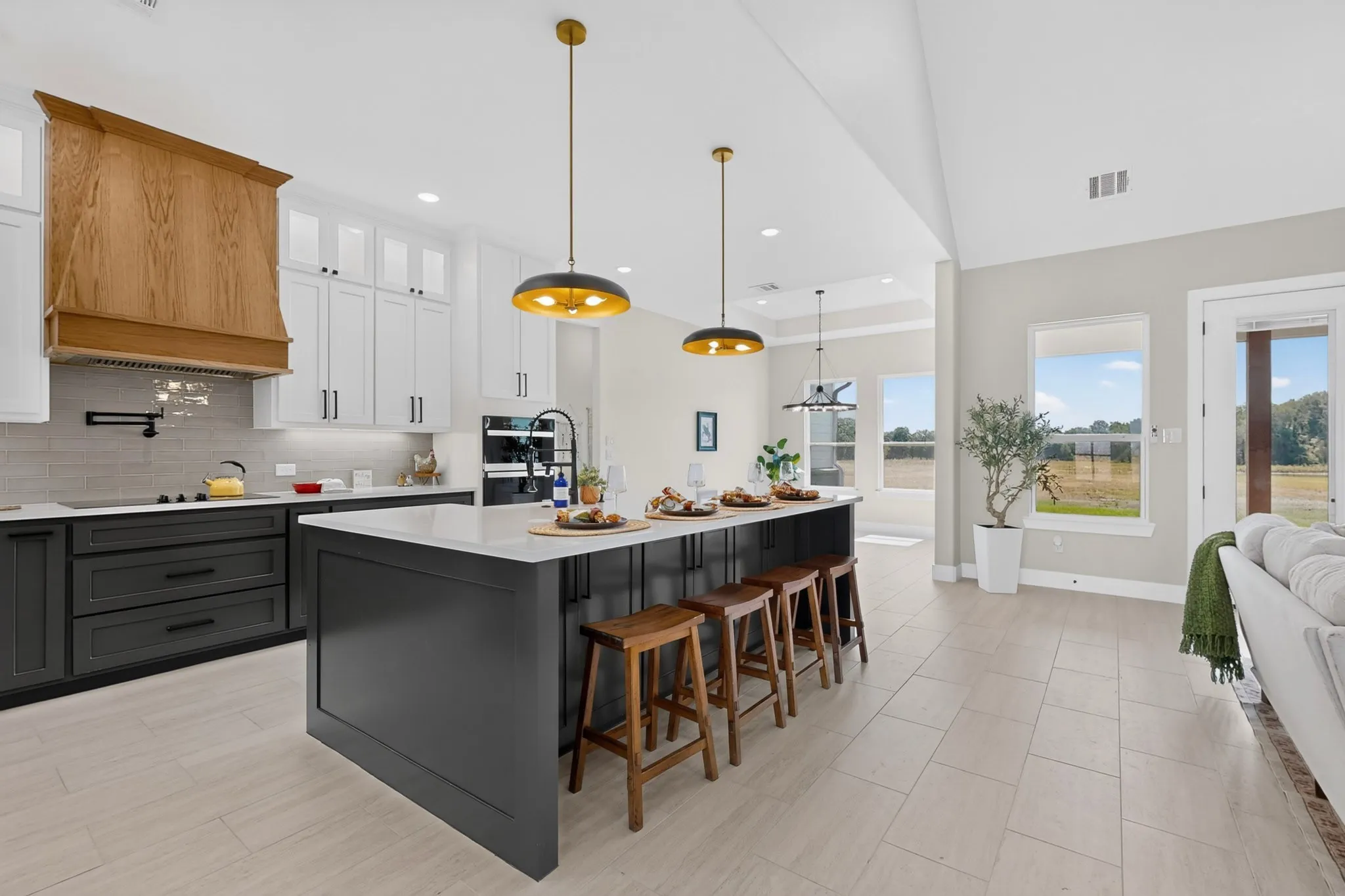 Spacious kitchen featuring an expansive island with seating, built-in stainless steel appliances, a wood-finish range hood, and white upper cabinetry