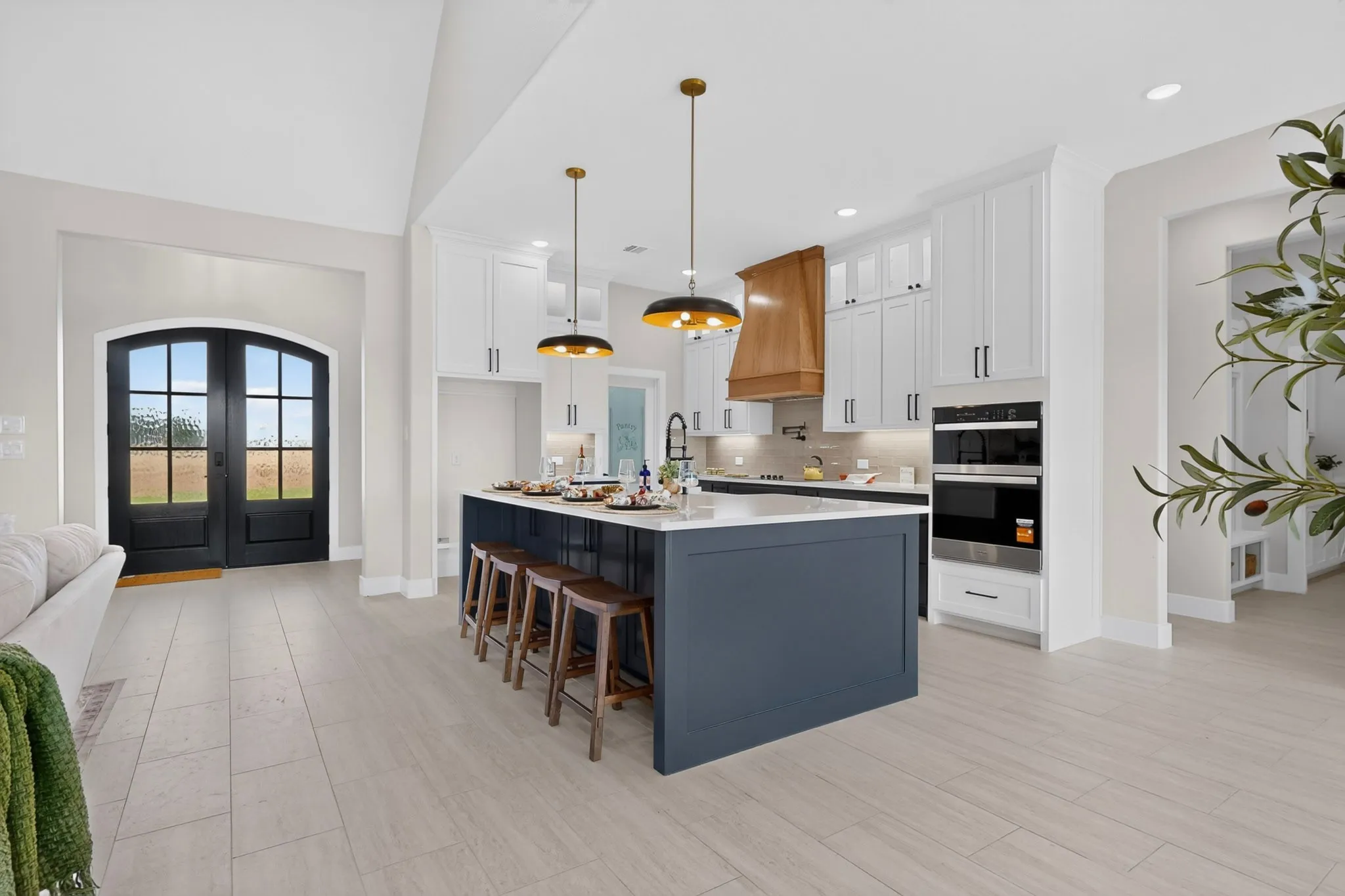 Arched double entry doors, wood-finish flooring, kitchen island with seating, built-in double oven, and pendant lighting