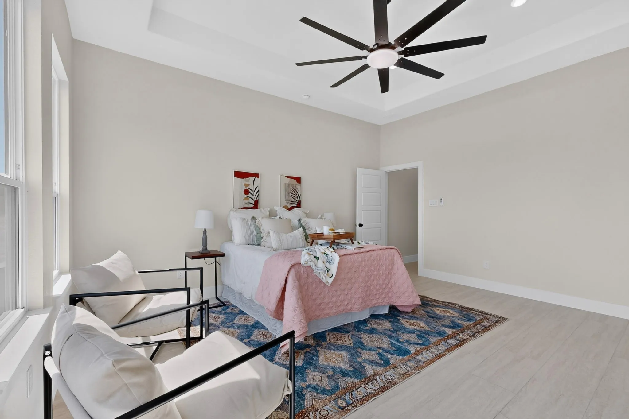 Tray ceiling with a ceiling fan, light-toned walls, wood-finish flooring, and multiple windows