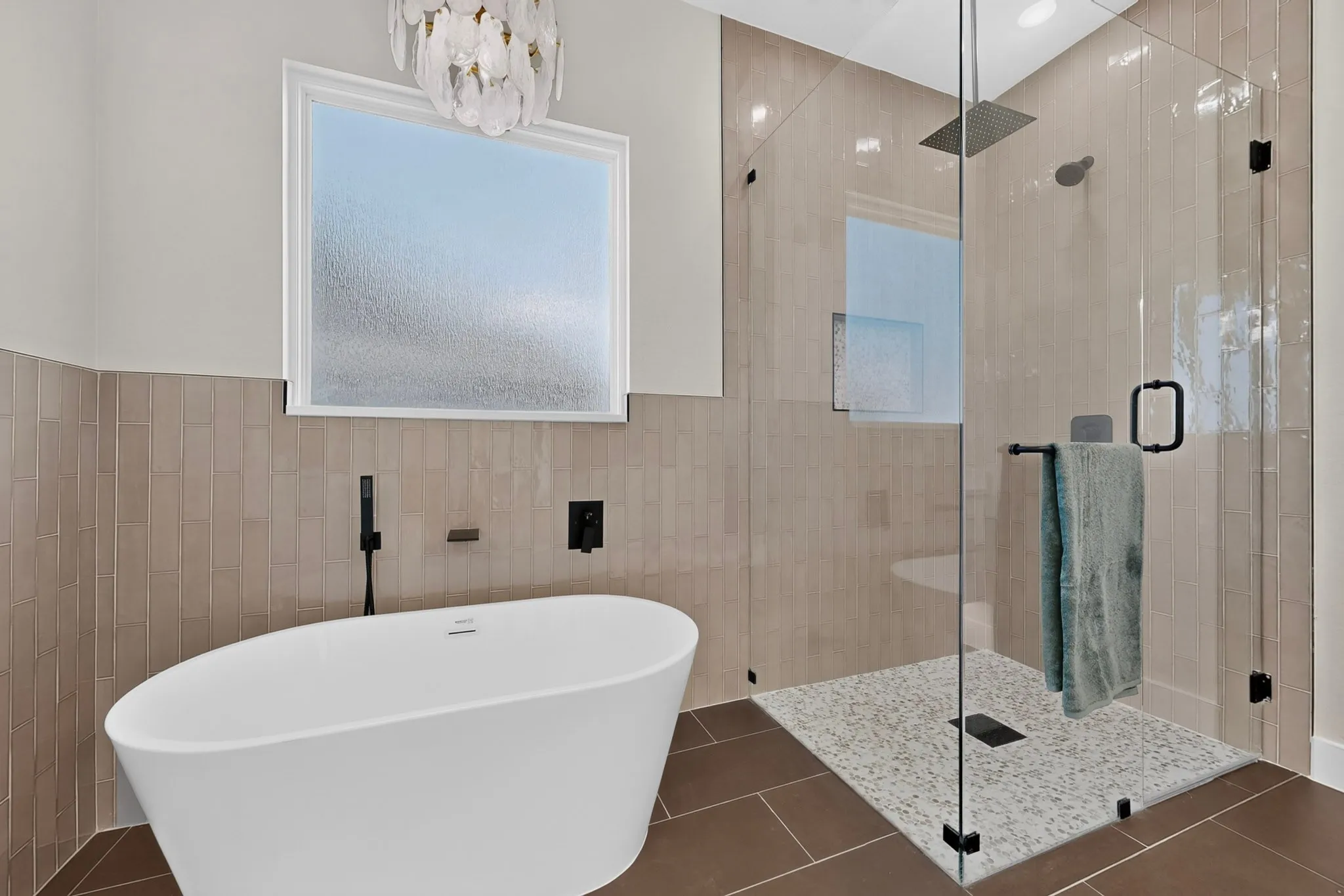 Freestanding soaking tub with matte black fixtures, glass-enclosed shower with rain showerhead, mosaic tile shower floor, and a decorative light fixture