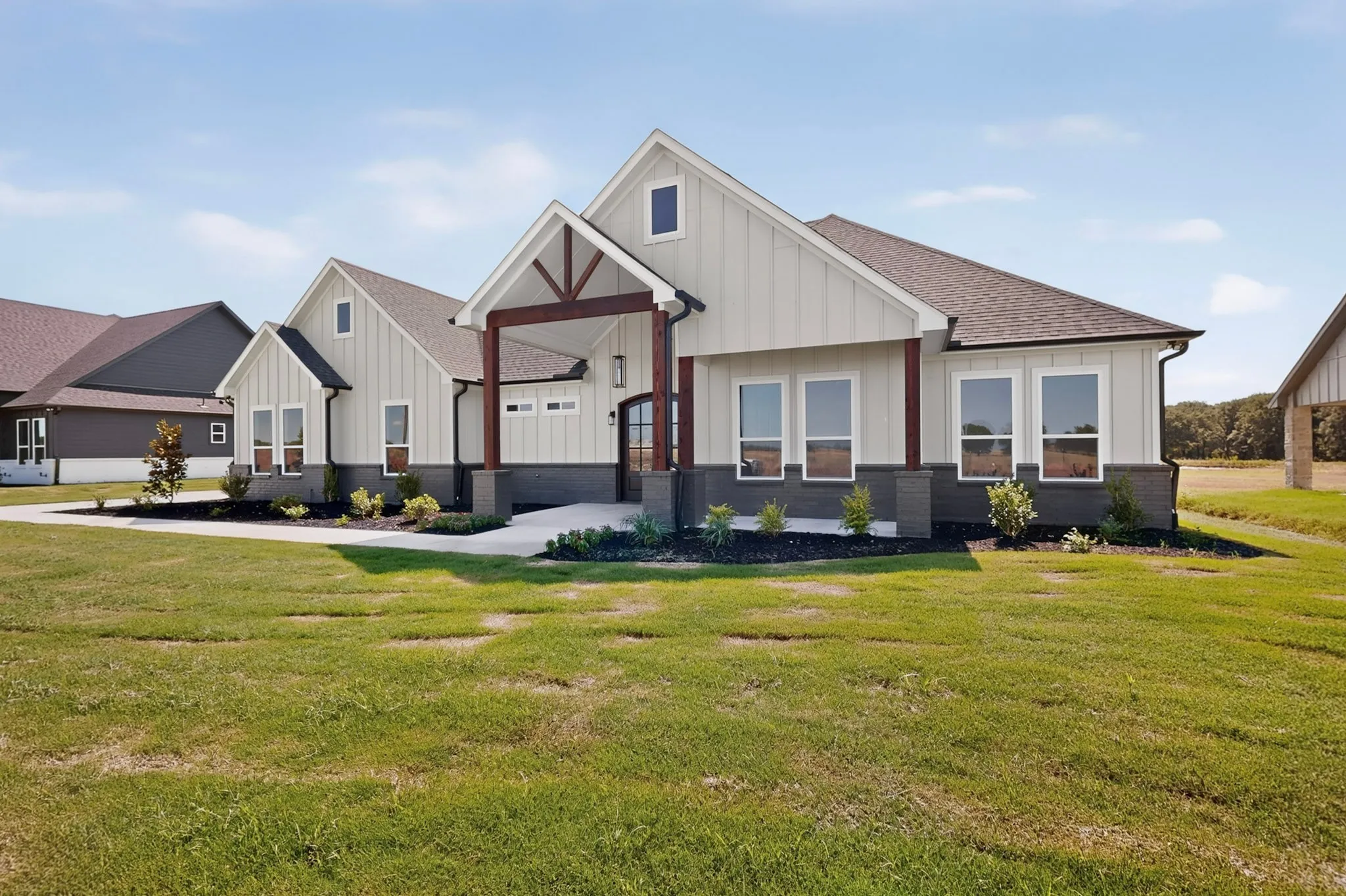 Contemporary farmhouse exterior featuring board and batten siding, dark shingle roof, stone foundation, and a covered entry with exposed wood beams