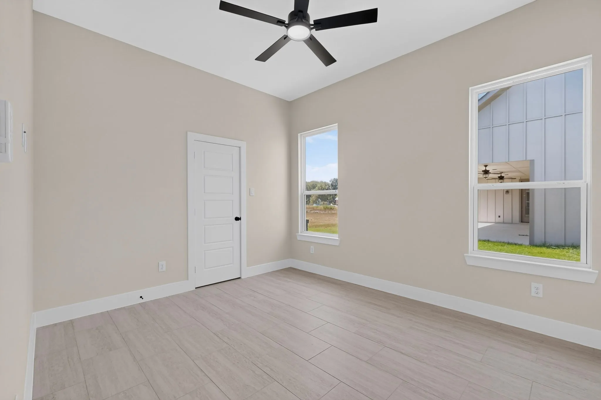 Vaulted ceiling with a black ceiling fan, two windows, five-panel interior door, and light wood-finish flooring