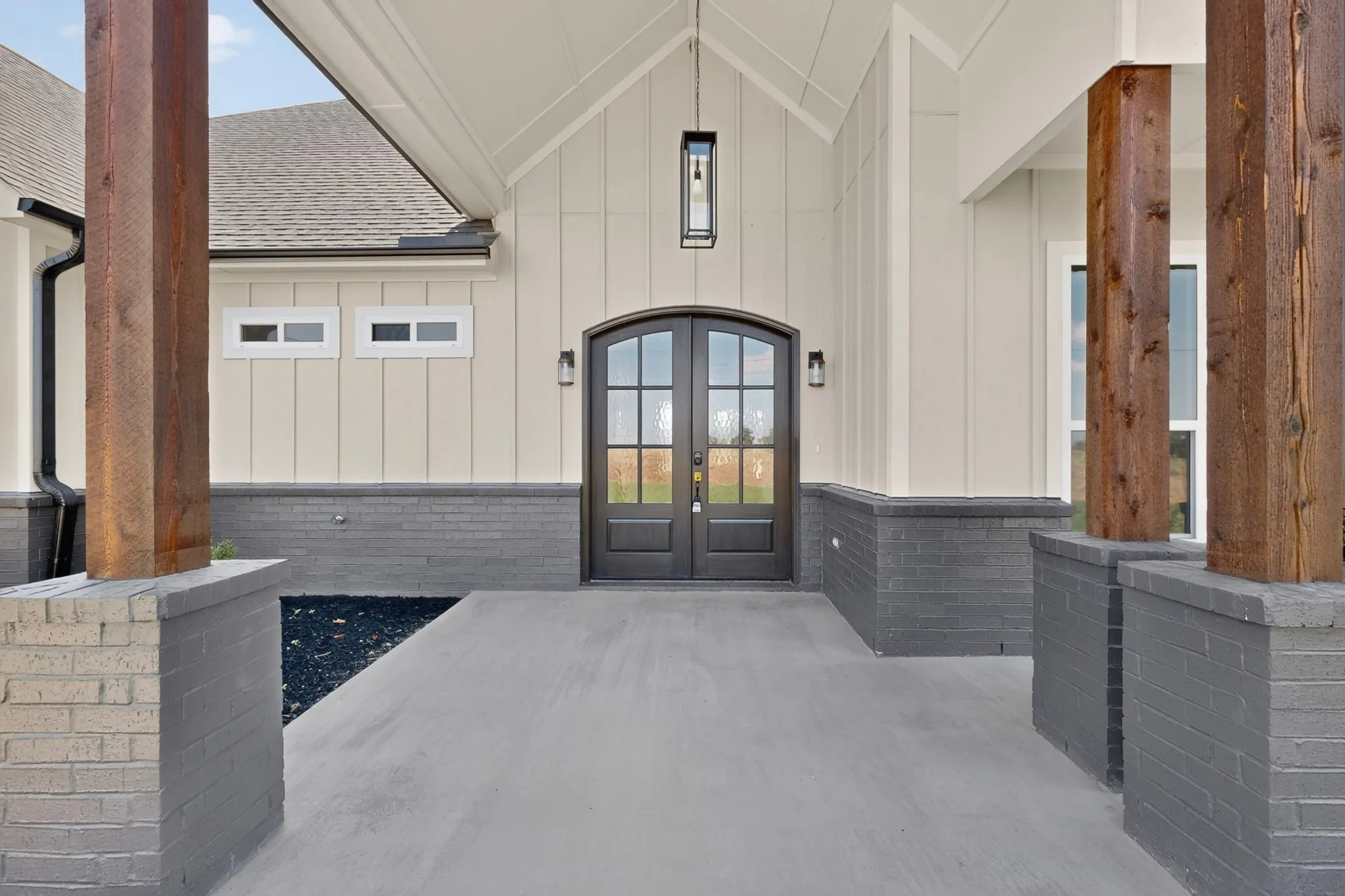 Covered entry with vaulted ceiling, wood-clad columns, dark brick accents, and a double-arched glass-panel door