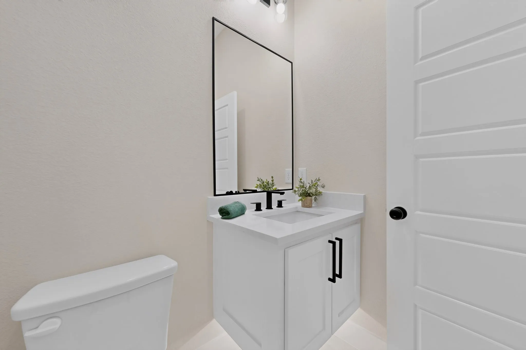White shaker-style vanity with a light-colored countertop and integrated sink, featuring a matte black faucet and cabinet hardware
