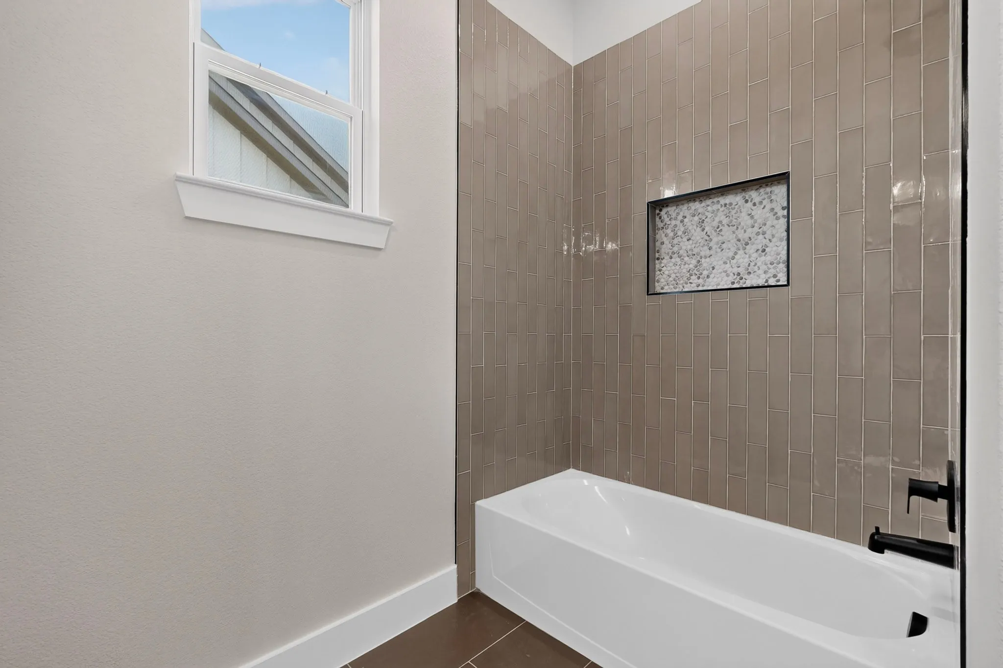 Built-in bathtub with matte black fixtures, full-height vertical tile surround, and a recessed tiled niche
