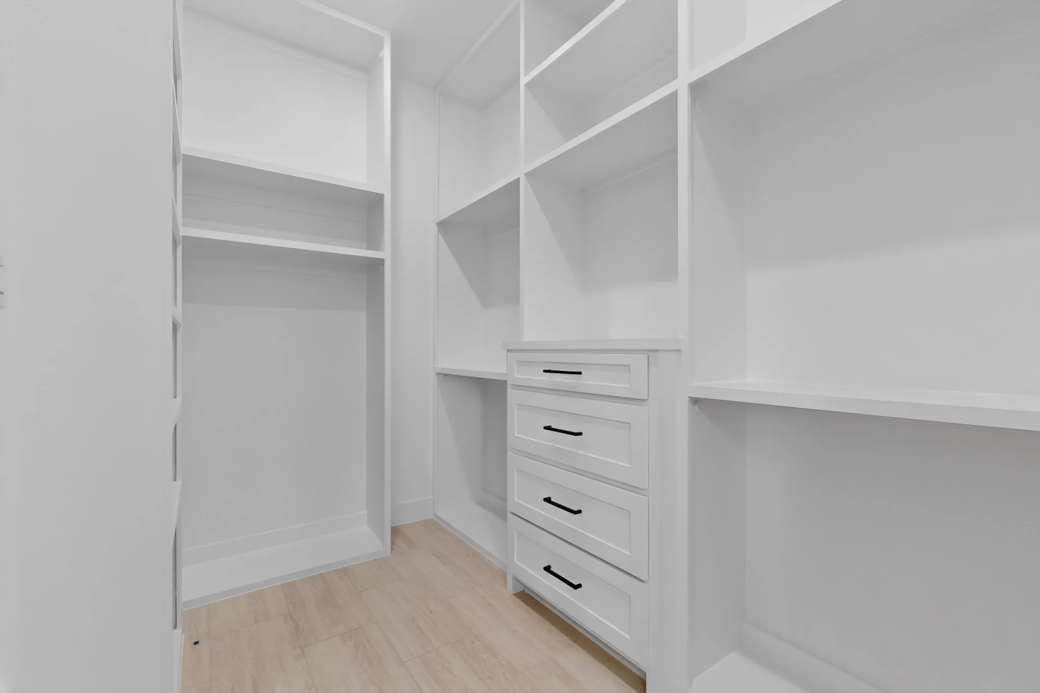 Custom closet system featuring built-in shelving, white cabinetry, and matte black hardware
