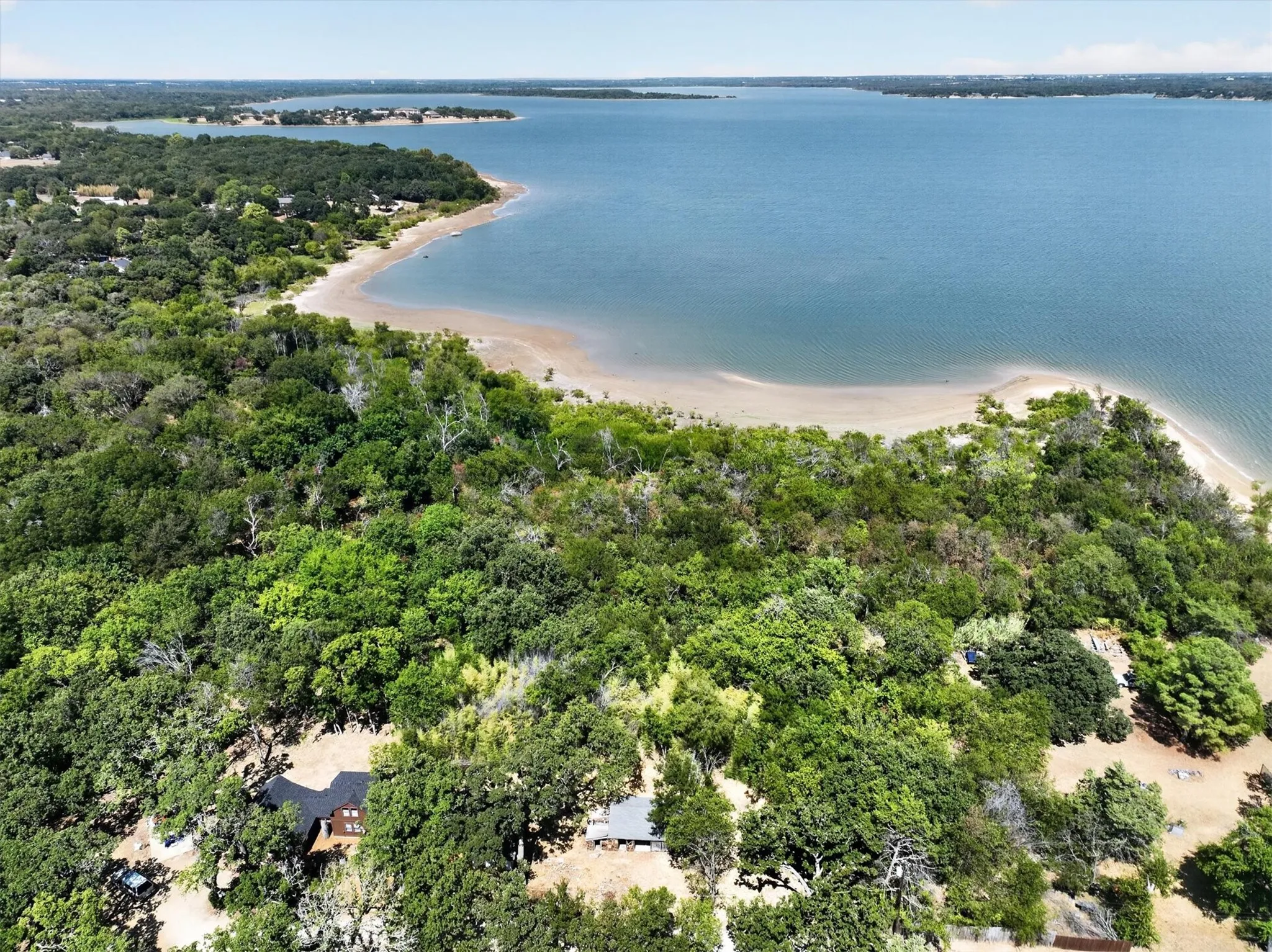 Expansive waterfront property featuring a natural sandy beach, mature trees, and a substantial body of water