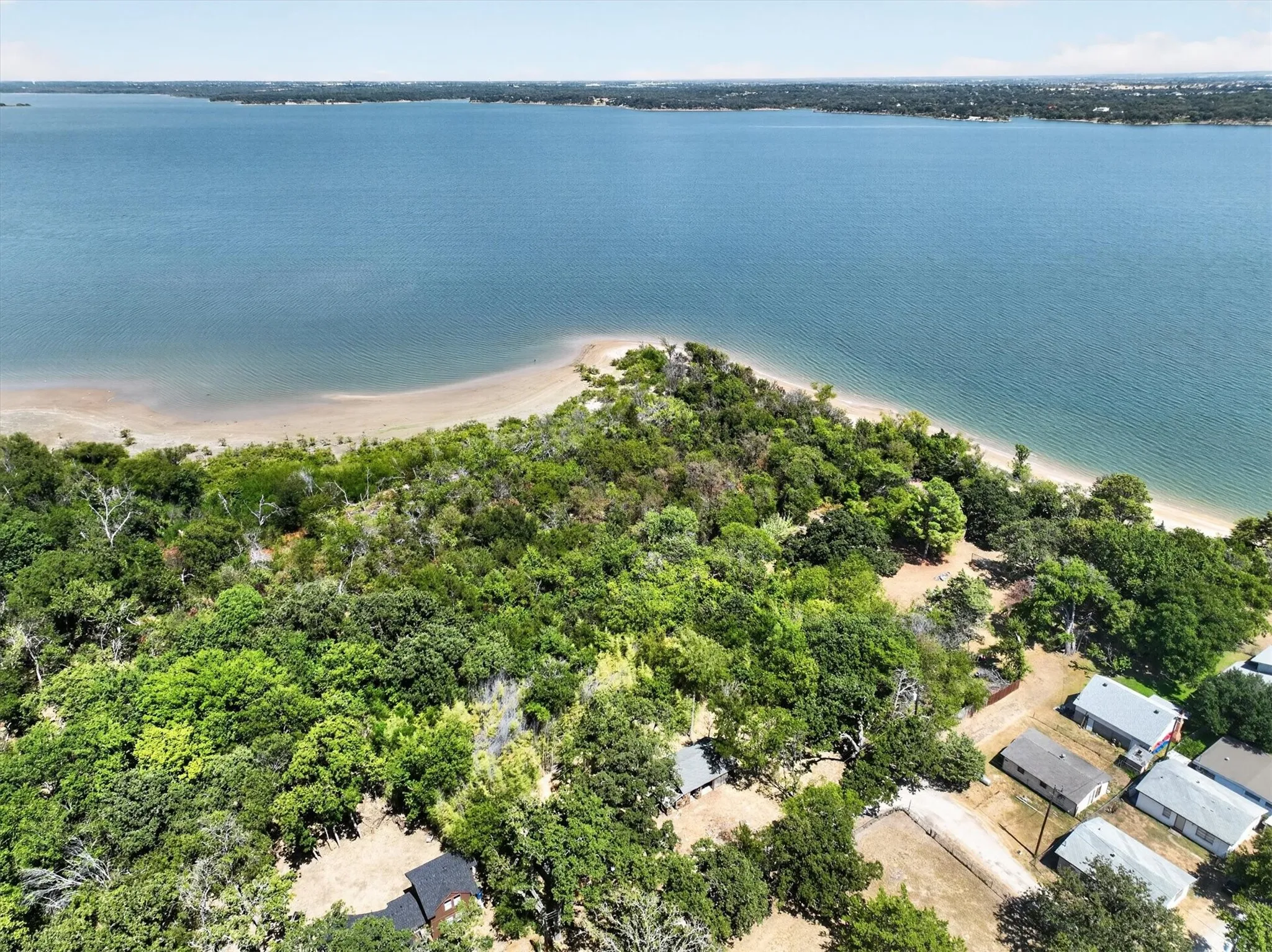 Expansive waterfront property featuring mature tree coverage, a sandy shoreline, and direct access to a large body of water