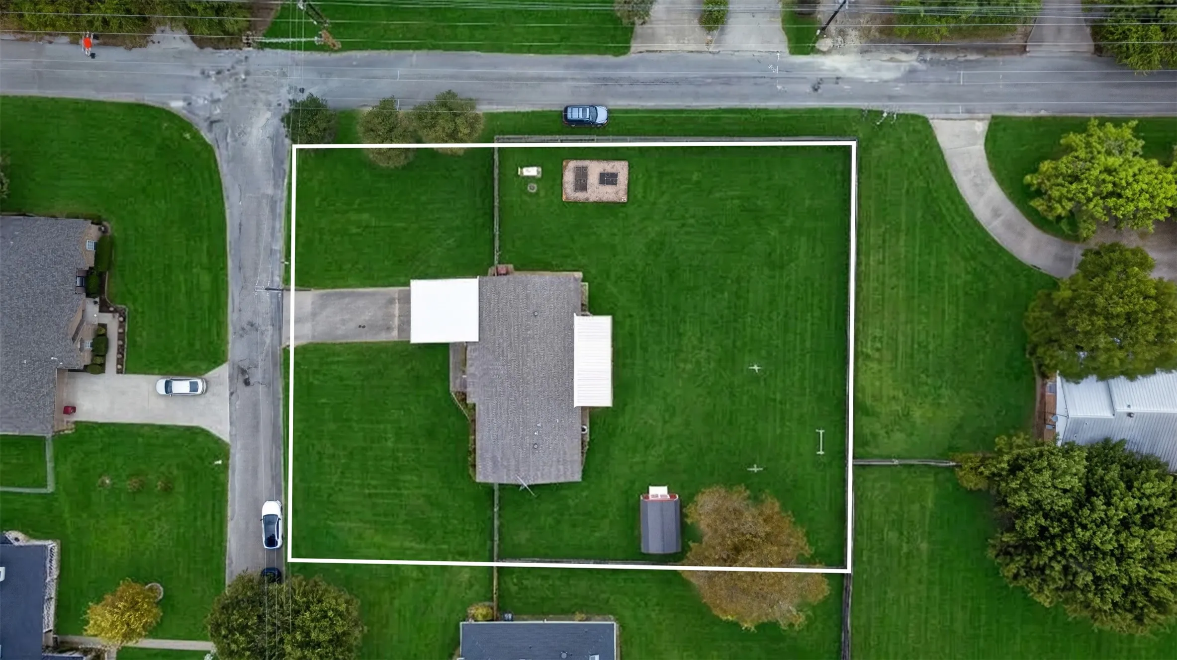 Expansive lot featuring a residential structure with an attached carport, a separate storage shed, and a paved driveway leading to a street