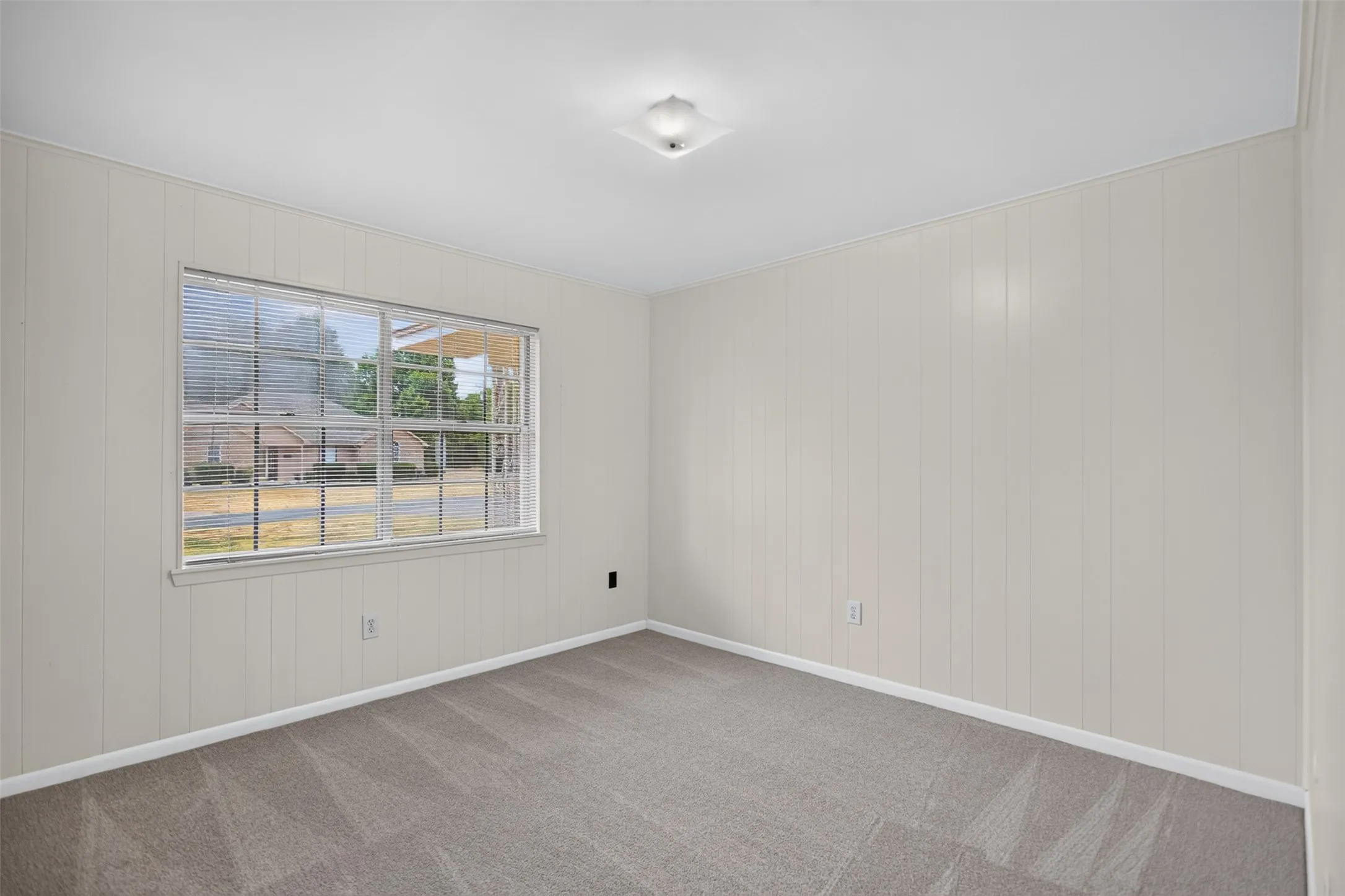 Spacious room featuring light-colored vertical paneling, neutral carpet, and a large window with horizontal​​‌​​​​‌​​‌‌​‌‌​​​‌‌​‌​‌​‌​​​‌​​ blinds