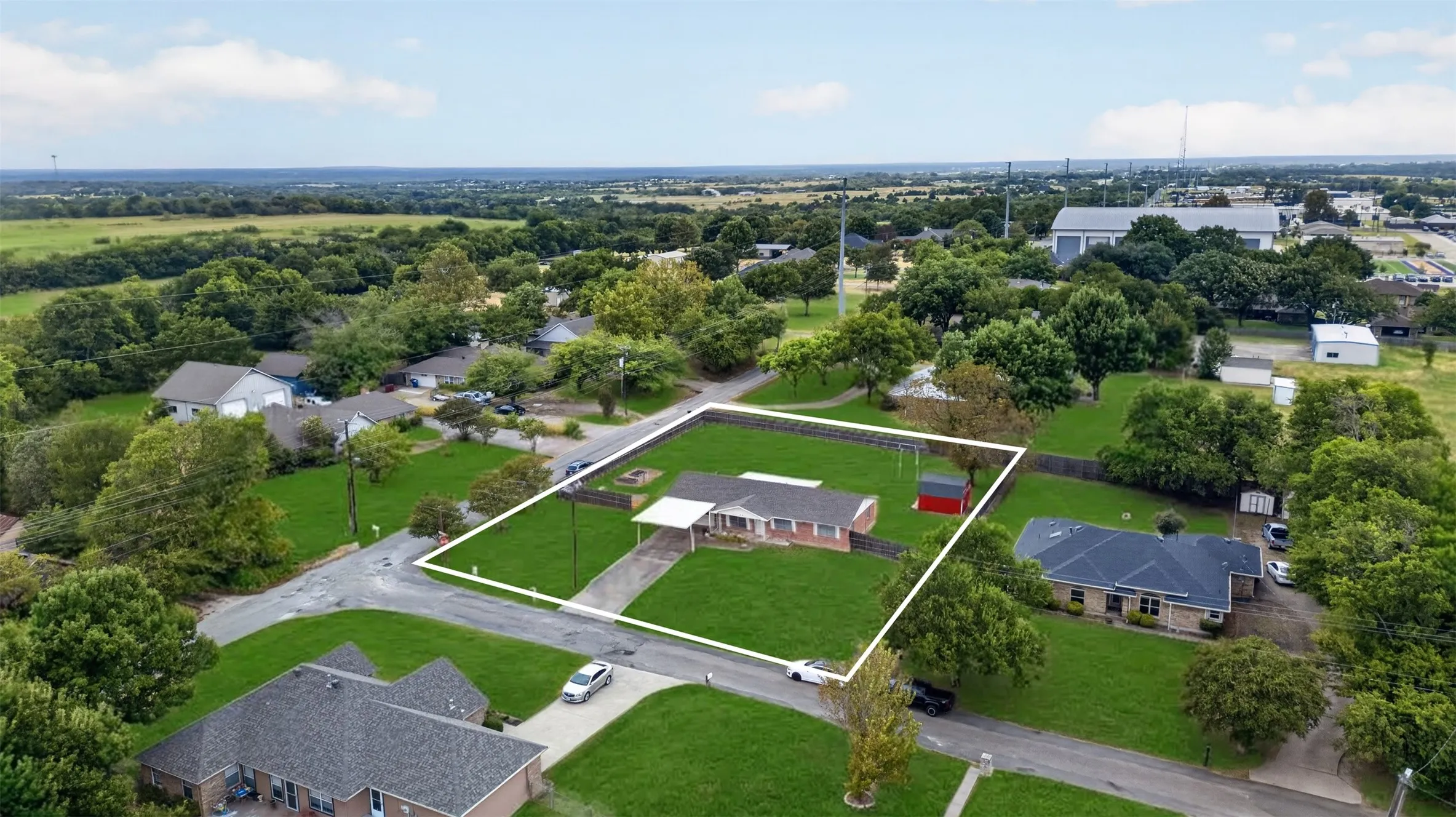 Single-story residence with a carport, mature landscaping, and a detached red outbuilding