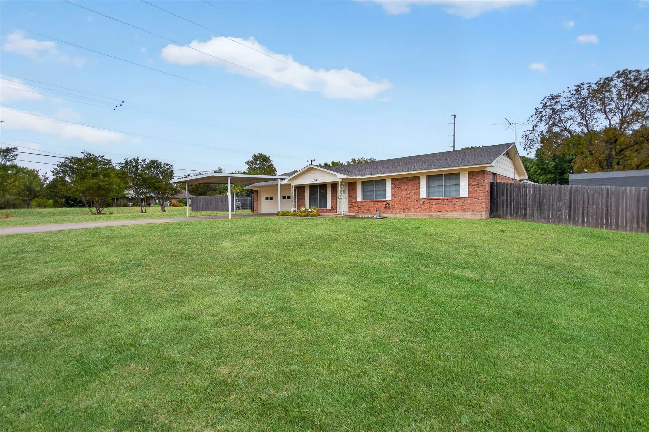 Brick exterior residence with a covered carport, attached garage, and a wood privacy fence