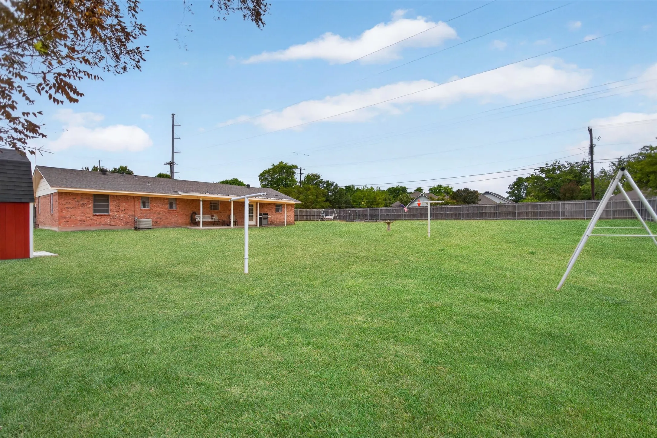Expansive green lawn with a red shed and a covered patio