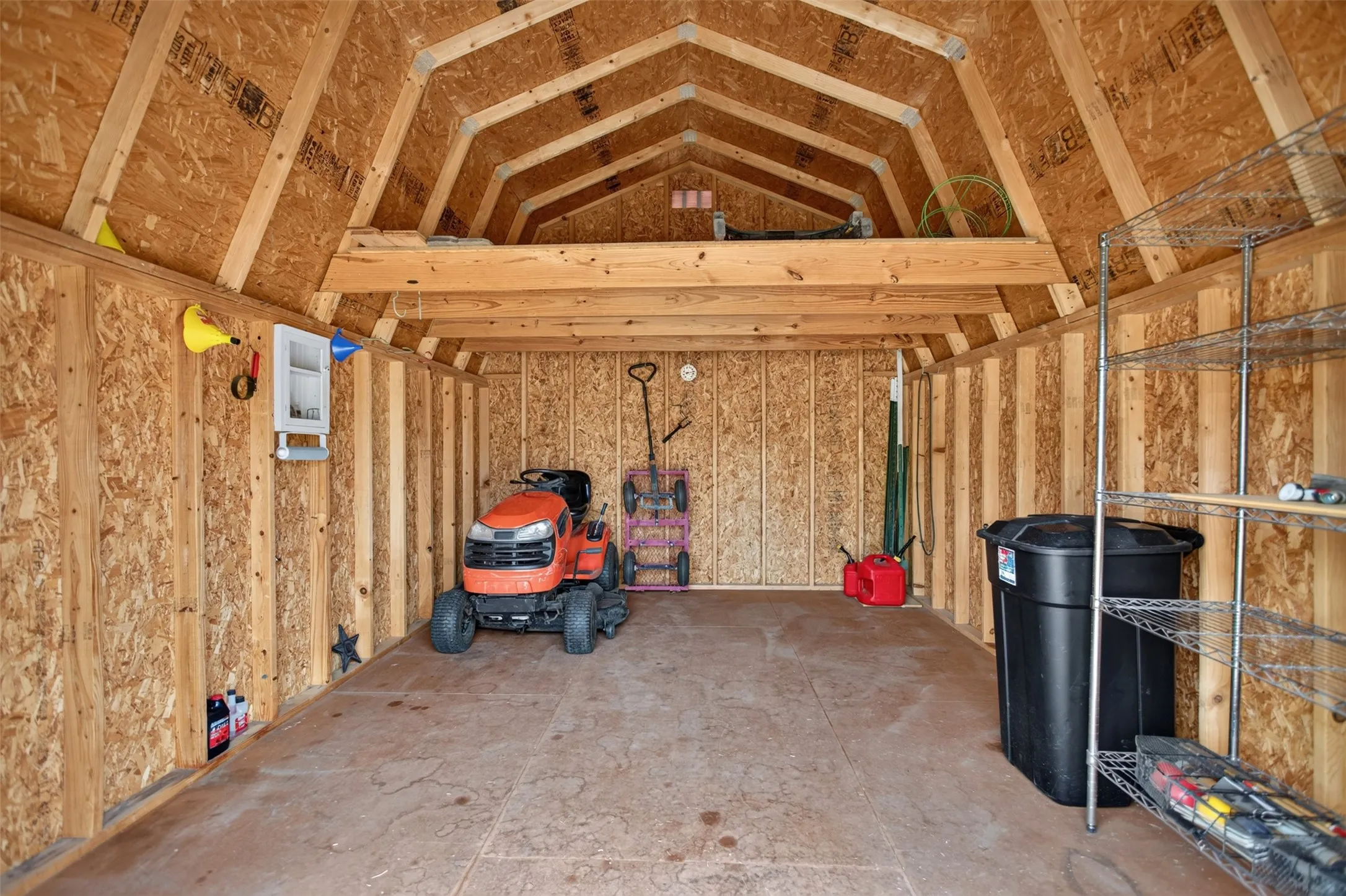 Spacious utility shed featuring plywood walls, exposed rafters, a built-in window, and an upper storage loft