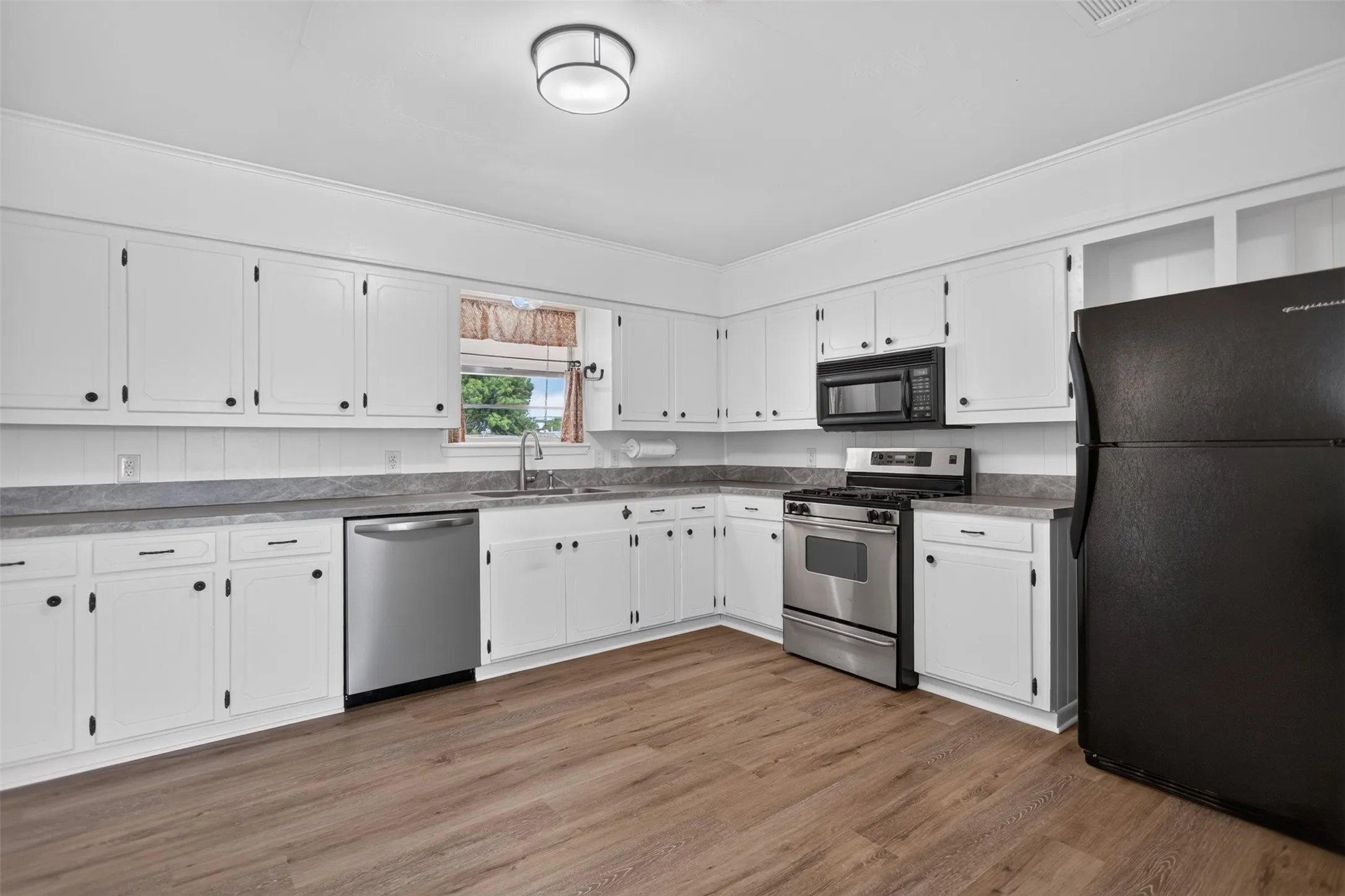 White cabinetry with black hardware, wood-finish flooring, stainless steel dishwasher, stainless steel range, and built-in microwave