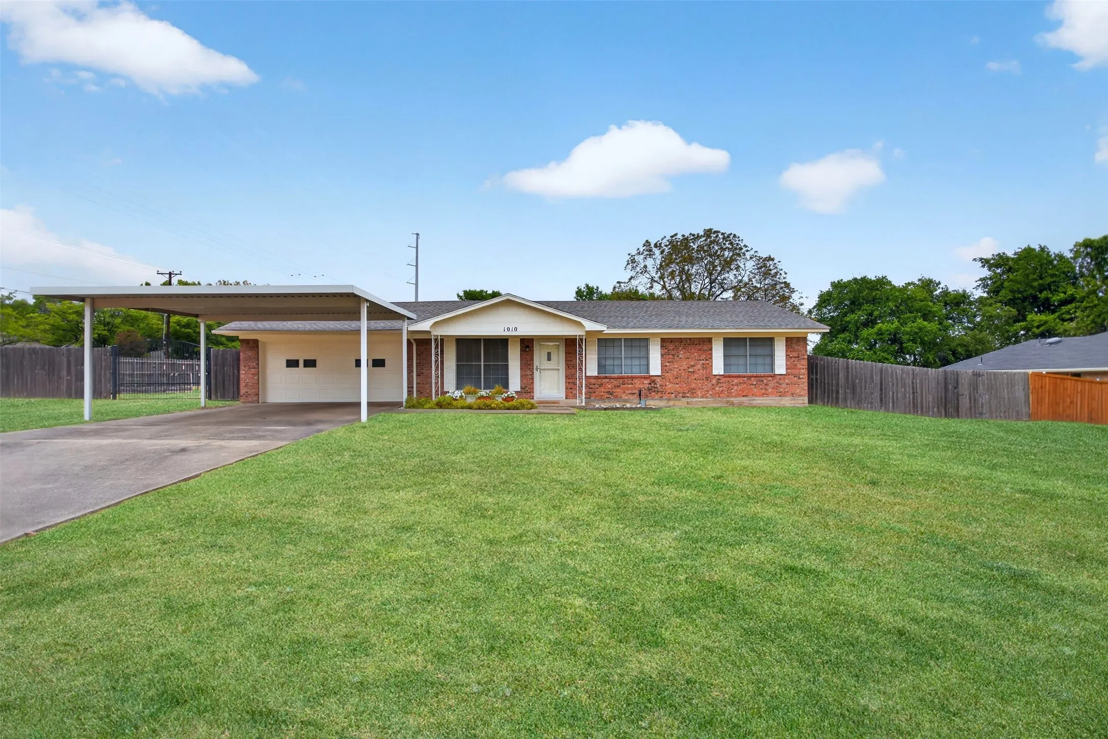 Brick exterior with white trim, attached carport, two-car garage, and a fenced backyard