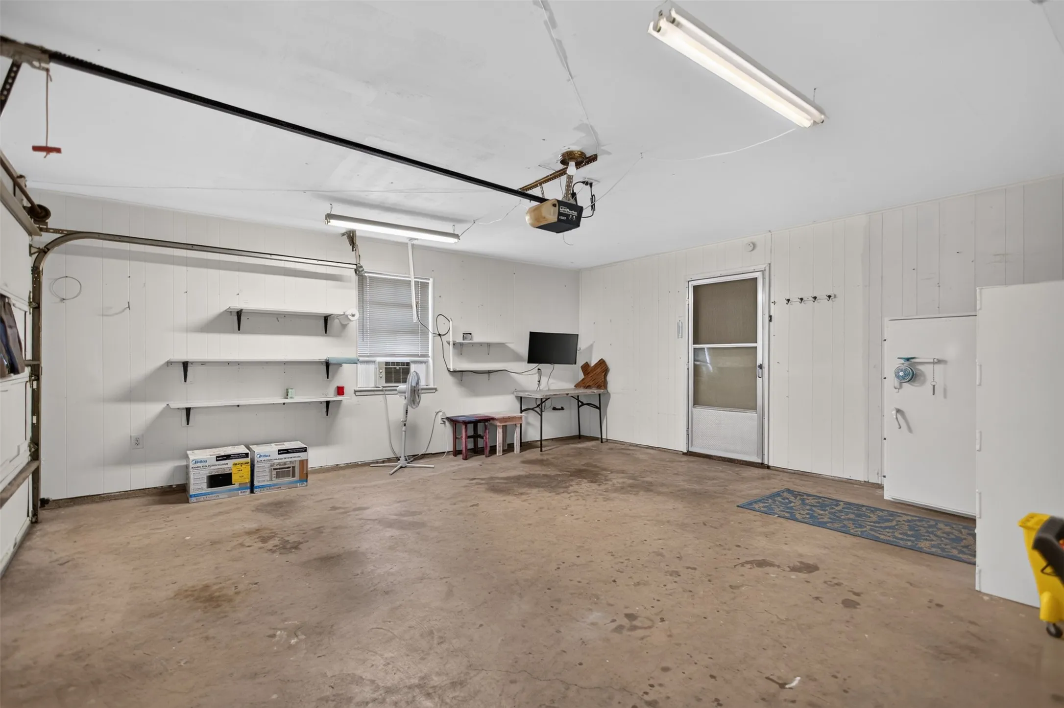 Garage space featuring a concrete floor, built-in shelving, a side entry door, and fluorescent lighting fixtures