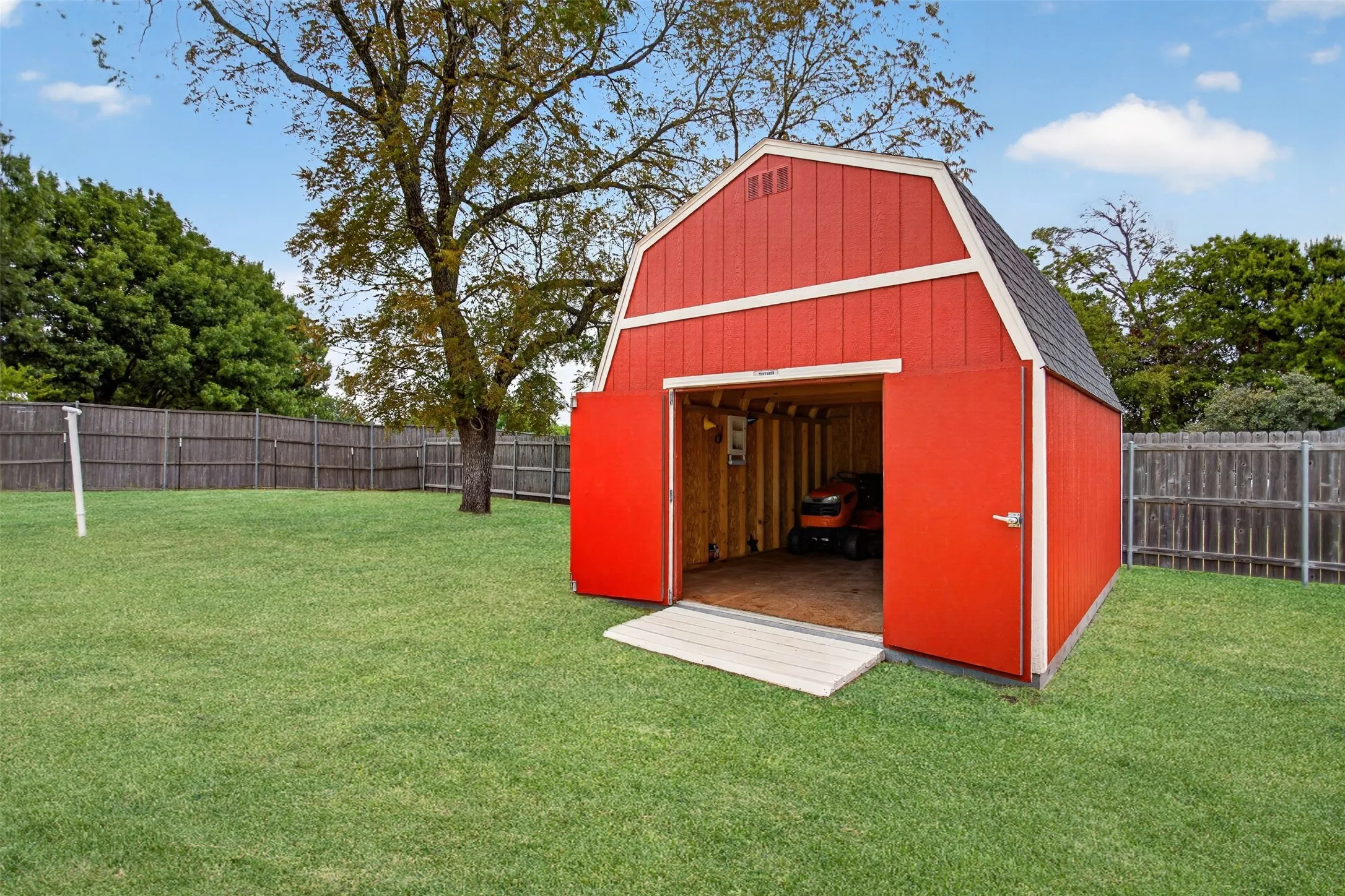 Expansive backyard featuring a manicured lawn, full privacy fencing, and a vibrant red barn-style shed with double doors