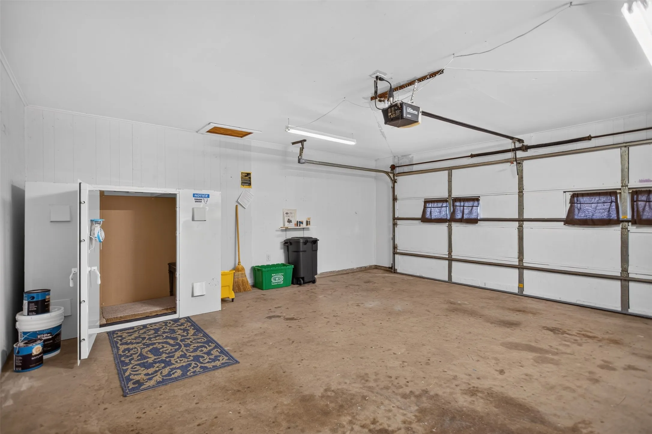 Concrete flooring, white painted walls, exposed garage door mechanism, fluorescent lighting