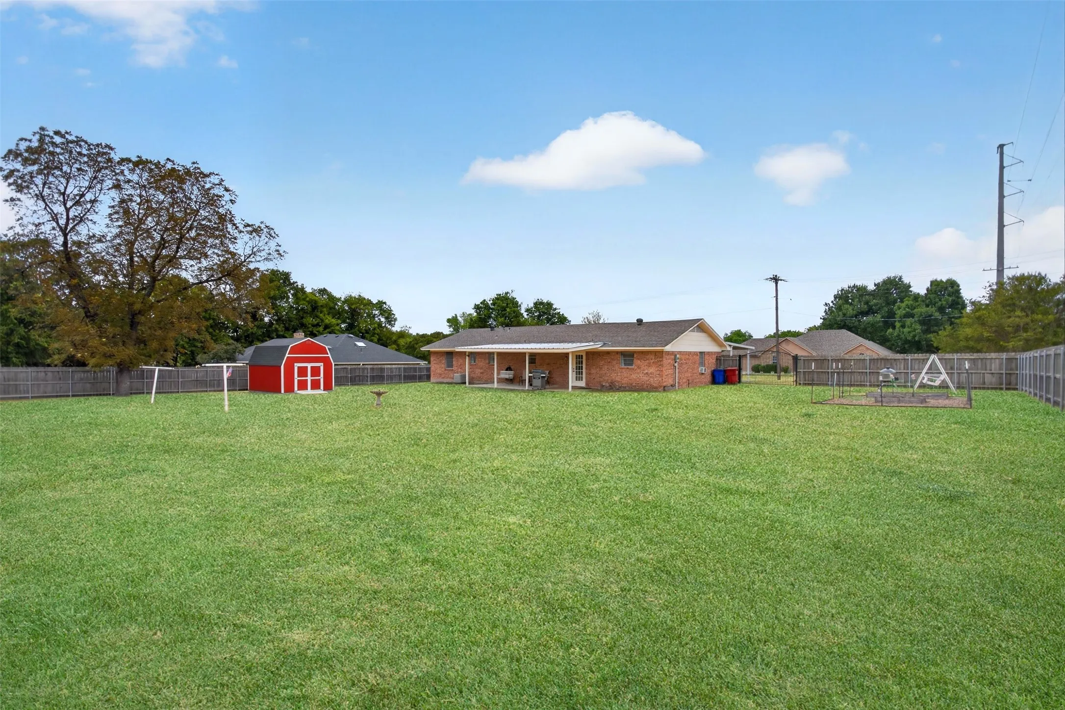 Expansive green lawn with a red barn-style shed, full privacy fencing, and a covered back patio