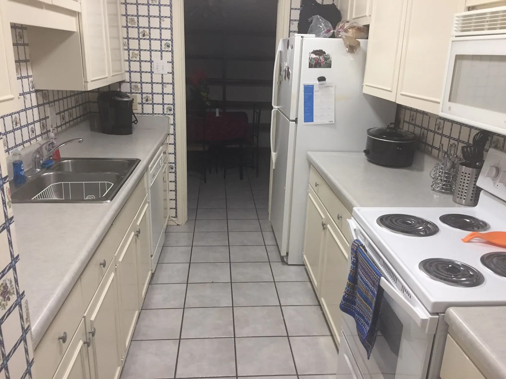 Galley kitchen featuring white cabinetry, light countertops, a stainless steel double basin sink, and tile flooring
