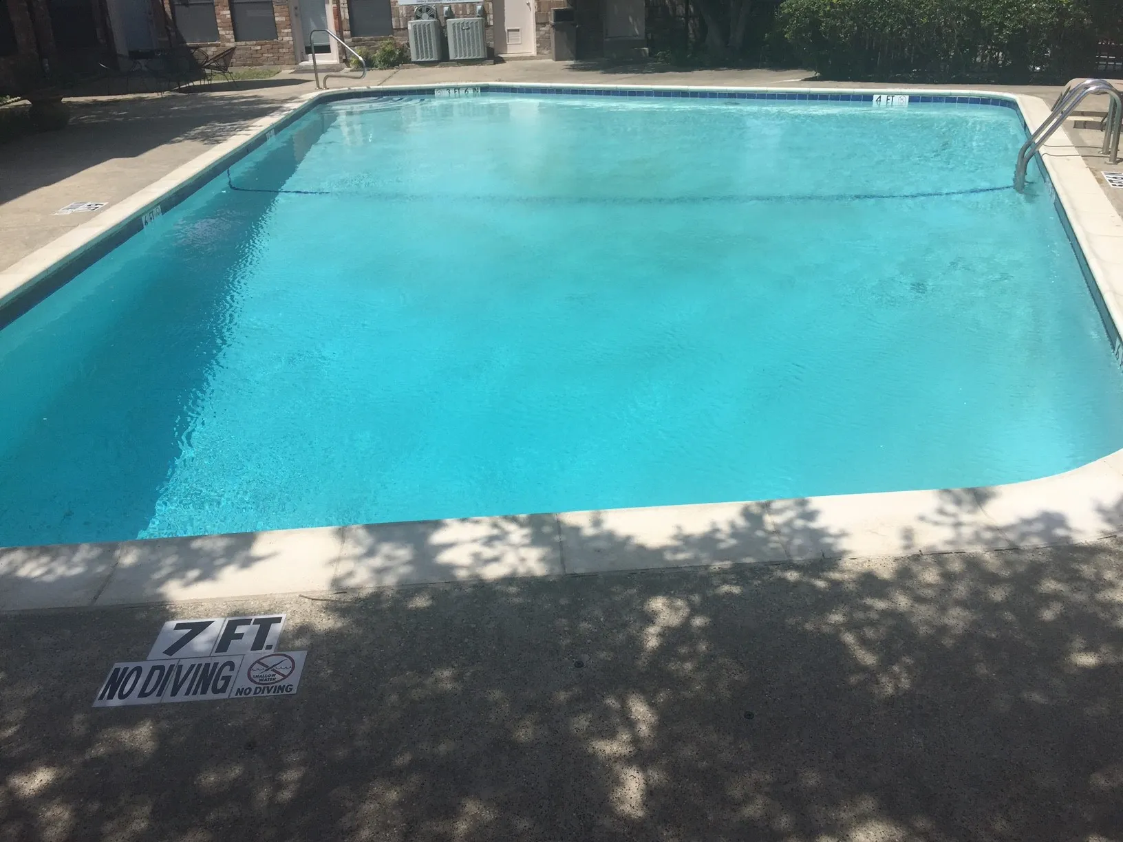 Rectangular swimming pool with light blue water, surrounded by concrete decking and white coping