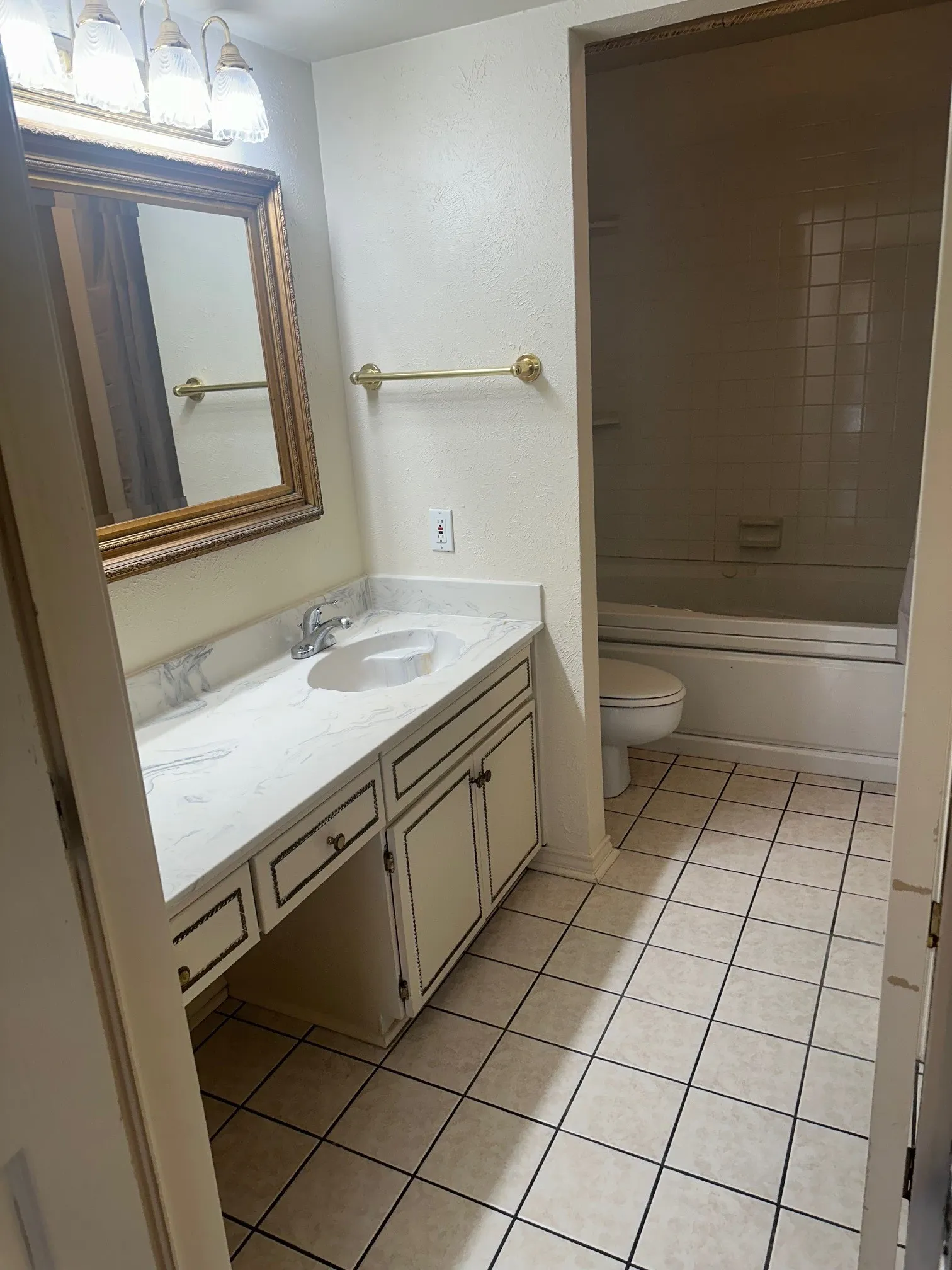 Vanity with integrated sink, white countertop, and gold-framed mirror