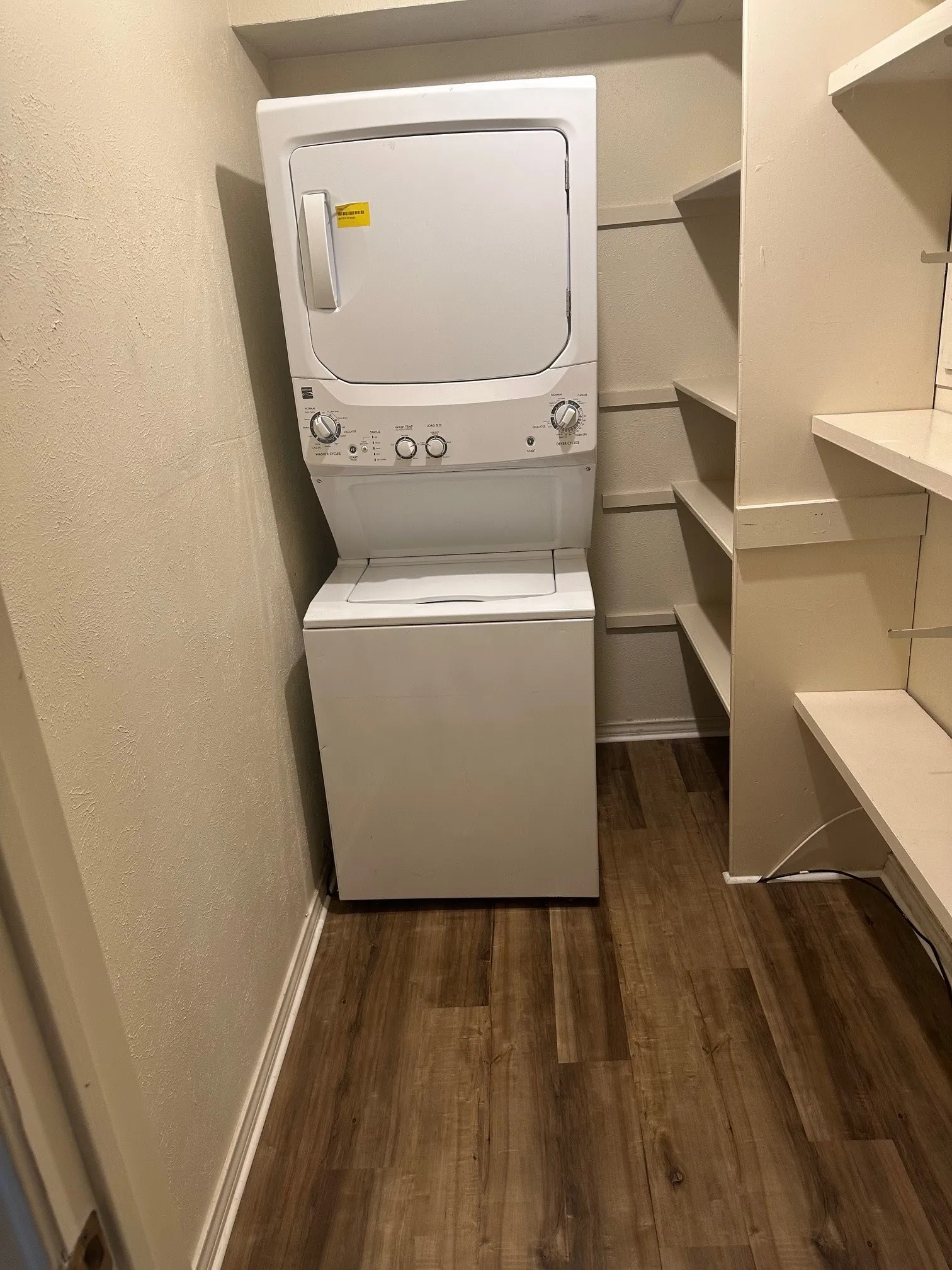 Compact laundry area featuring a stacked washer and dryer, wood-finish flooring, and built-in shelving