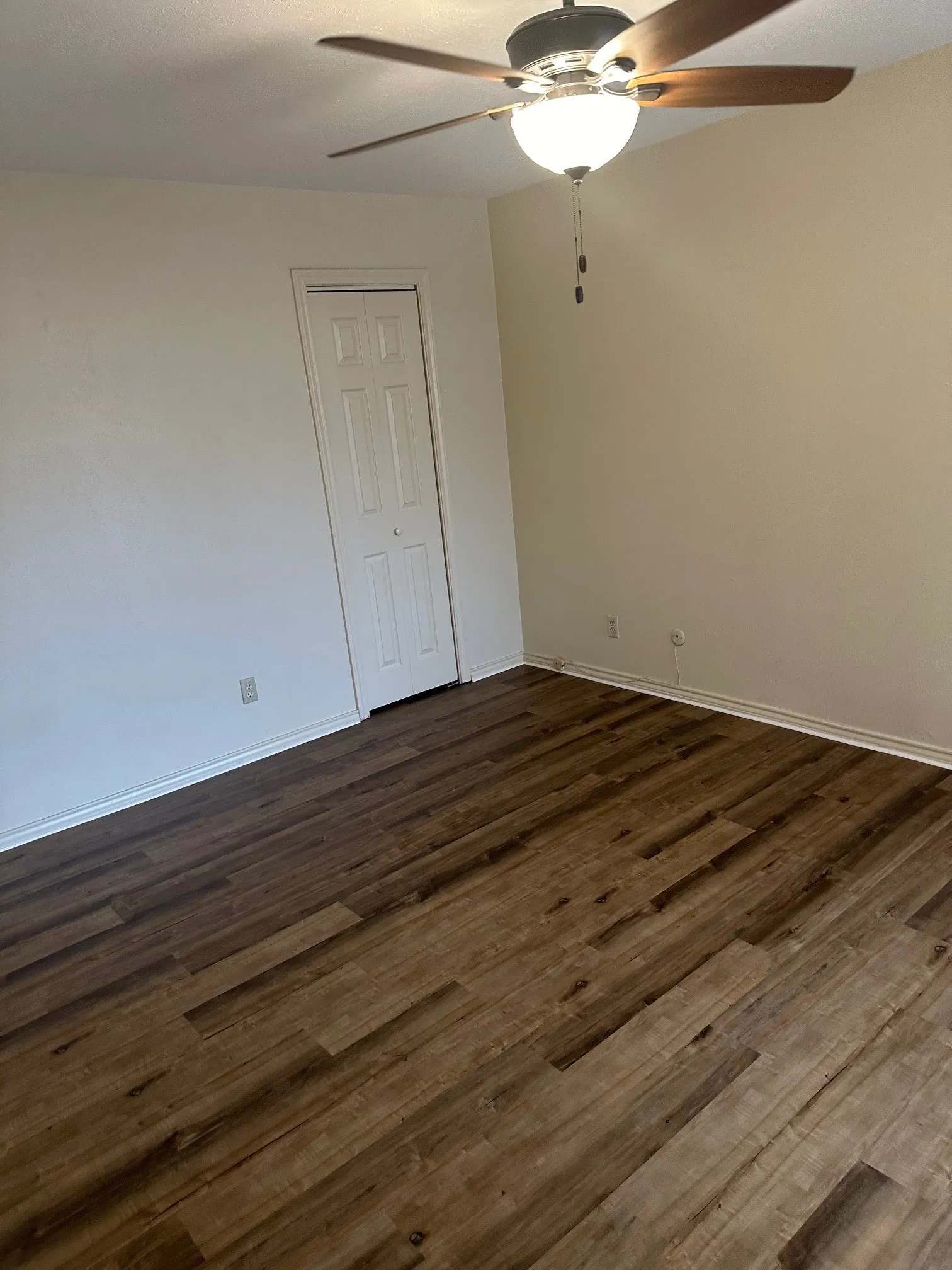 Wood-finish flooring throughout, bright white walls, and a ceiling fan with integrated lighting