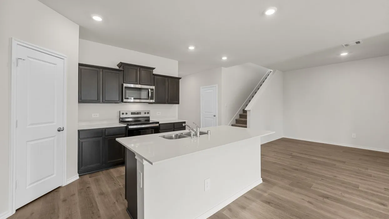 Kitchen with dark wood cabinetry, stainless steel appliances, white countertops, and a center island with sink