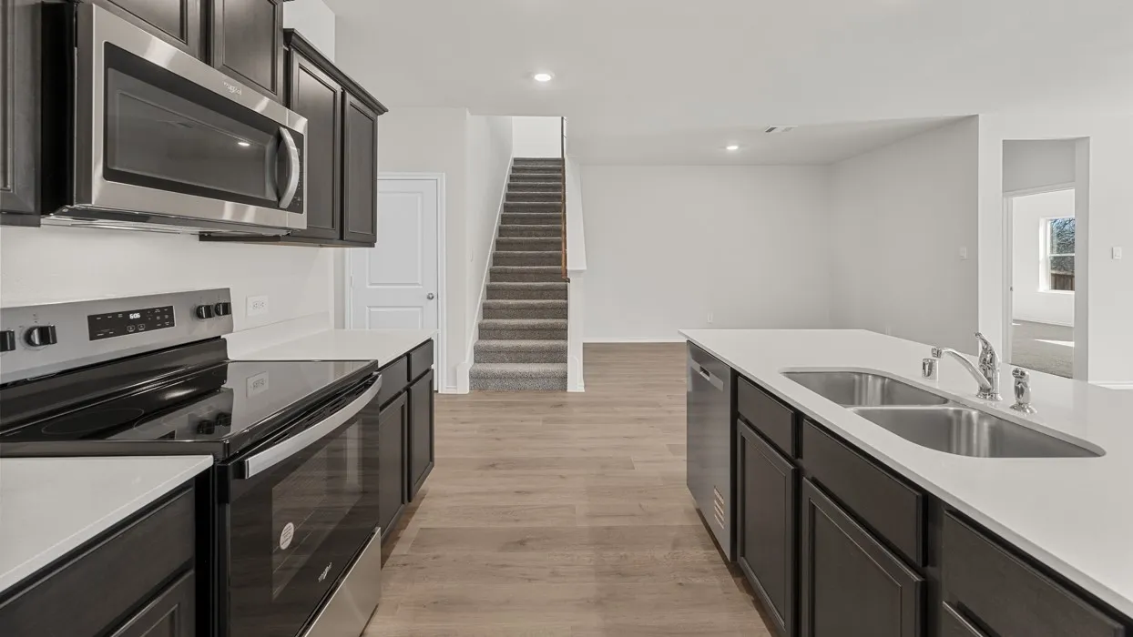 Kitchen featuring dark wood cabinetry, stainless steel appliances, light countertops, and an undermount double basin sink