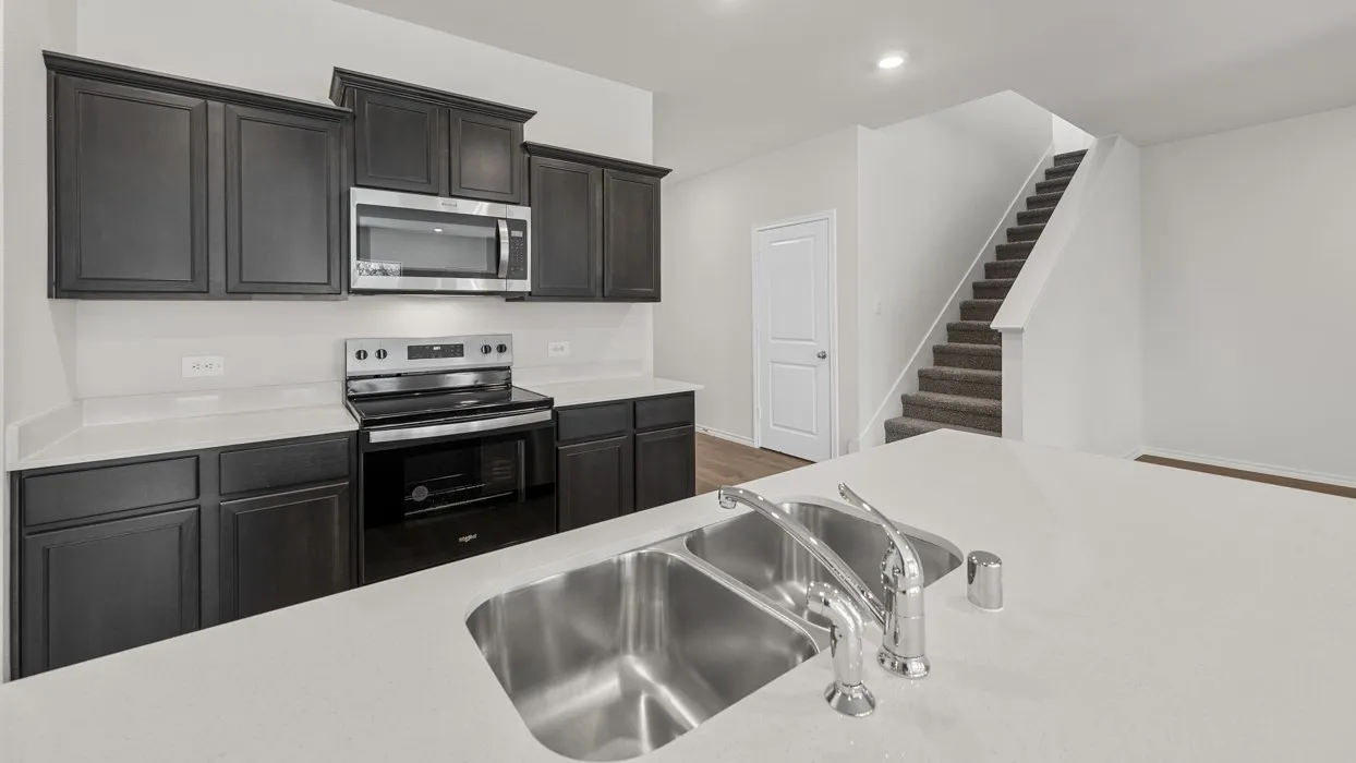 Kitchen featuring dark wood-finish cabinetry, stainless steel appliances, and light-toned countertops with a double basin sink