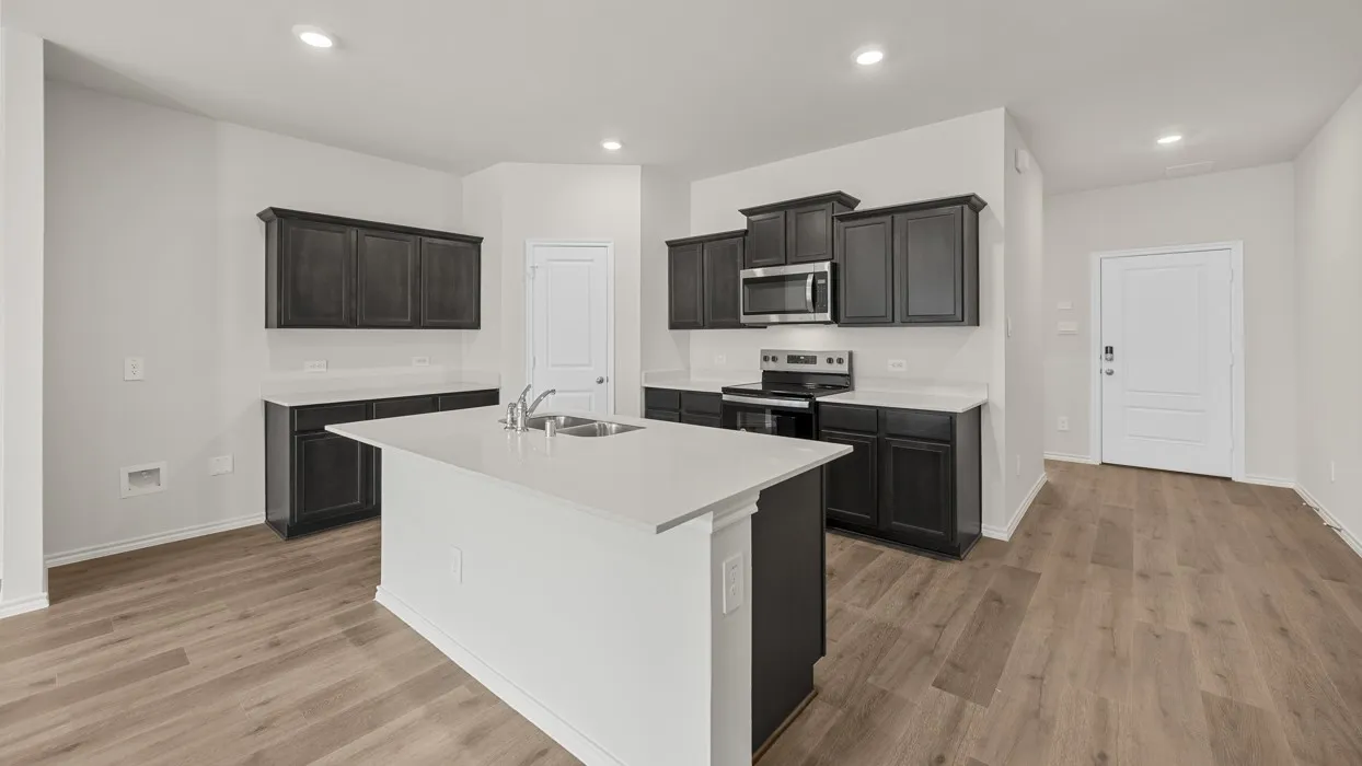 Kitchen featuring dark cabinetry, white countertops, stainless steel appliances, a center island with sink, and wood-finish flooring