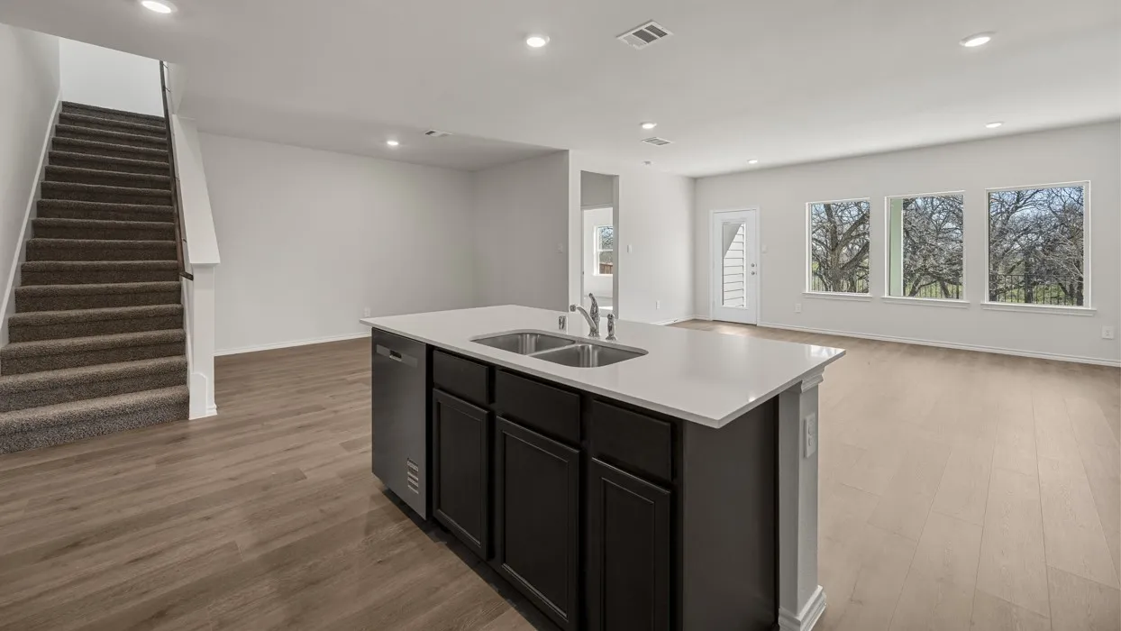 Open-concept living area featuring wood-finish flooring, recessed lighting, a kitchen island with dual sinks, and multiple windows