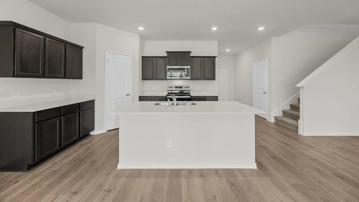 Kitchen featuring dark-toned cabinetry, light-toned countertops, and a central island with an integrated sink