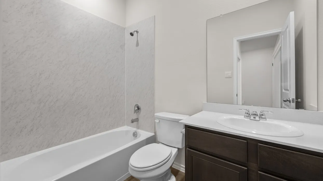 White bathtub with an integrated shower, white vanity countertop, undermount sink, and a dark wood-finish vanity with cabinet storage