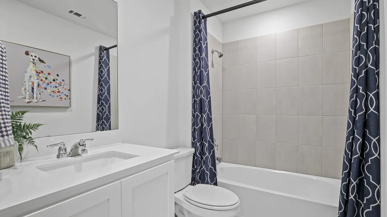 Integrated bathtub and shower with tiled surround, white vanity, built-in sink, and chrome fixtures