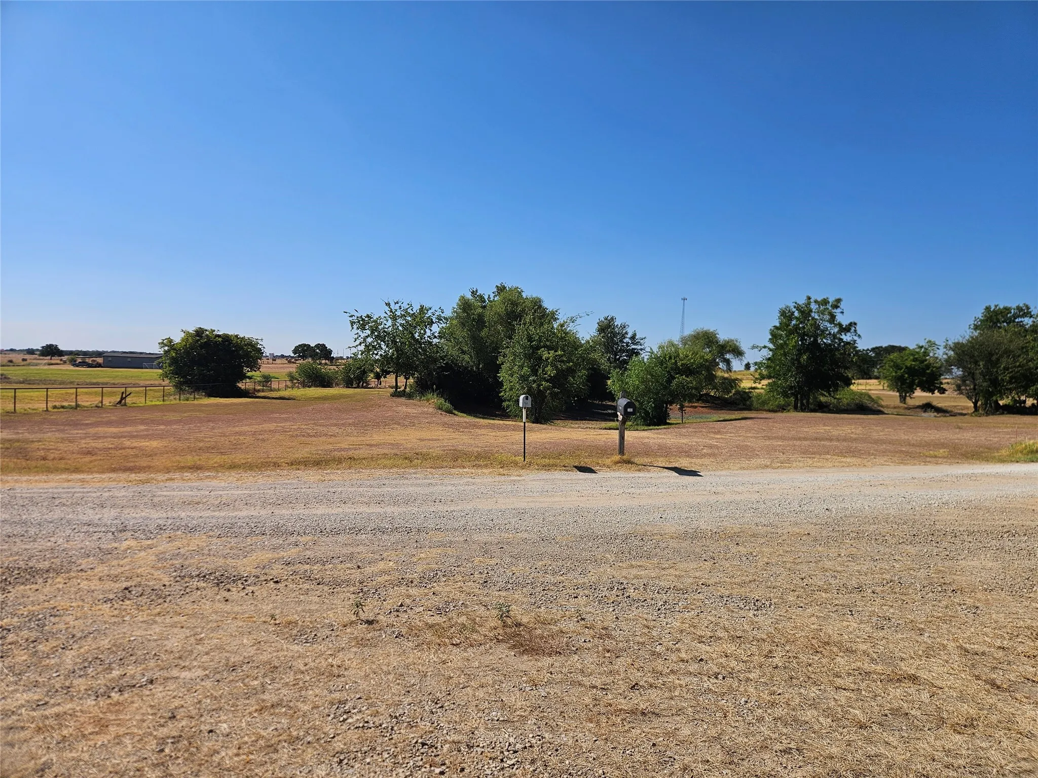 Gravel road frontage leading to a property featuring mature trees and open land.