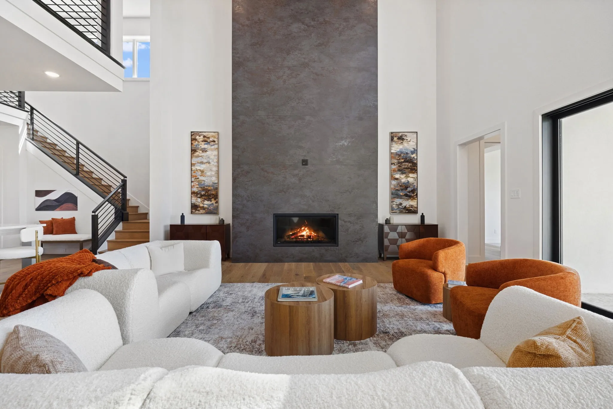 Double-height living space featuring a floor-to-ceiling fireplace, wood-finish flooring, and a contemporary open-tread staircase with black railing